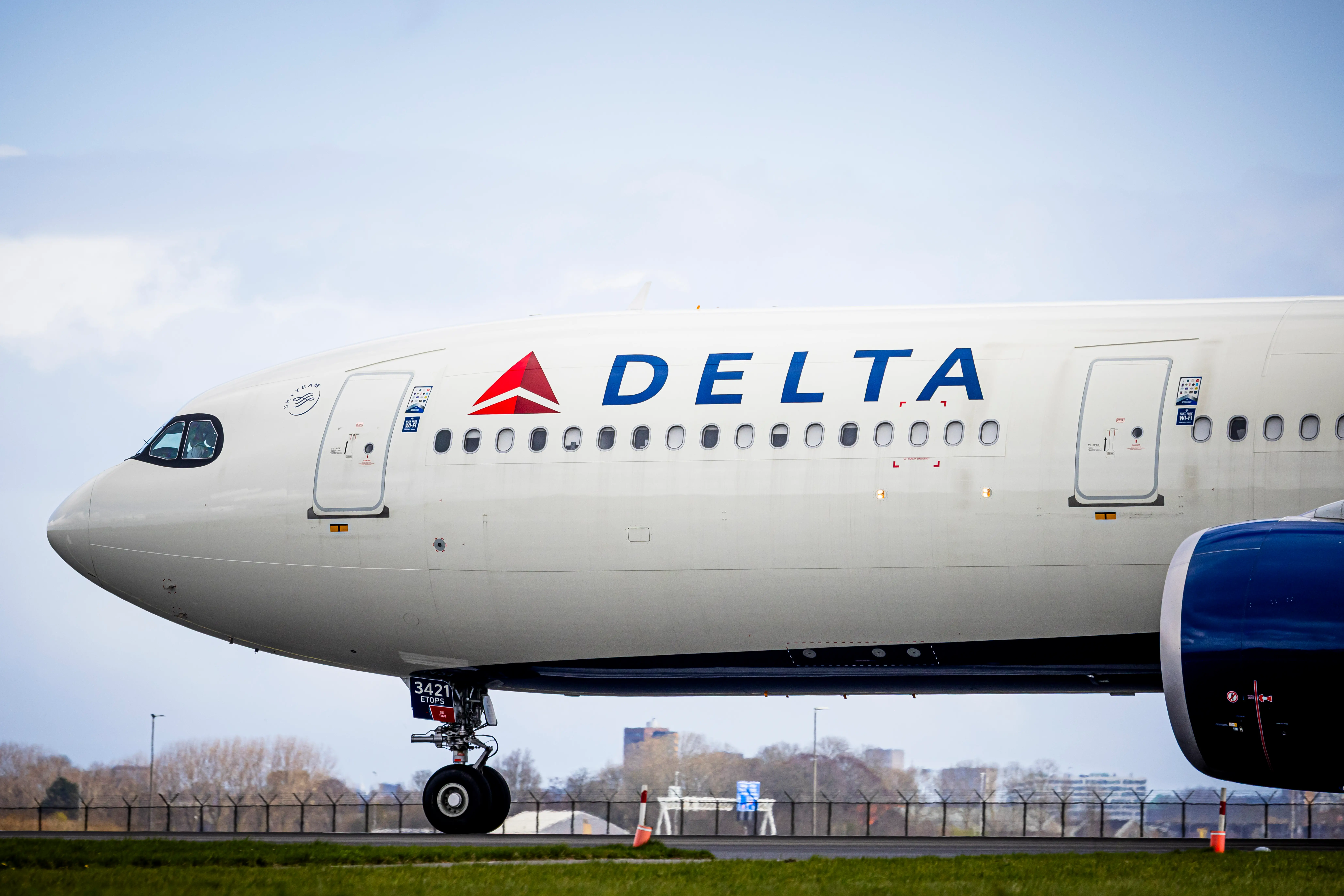 An airplane with a Delta symbol on it is parked on a grassy runway against a blue sky.