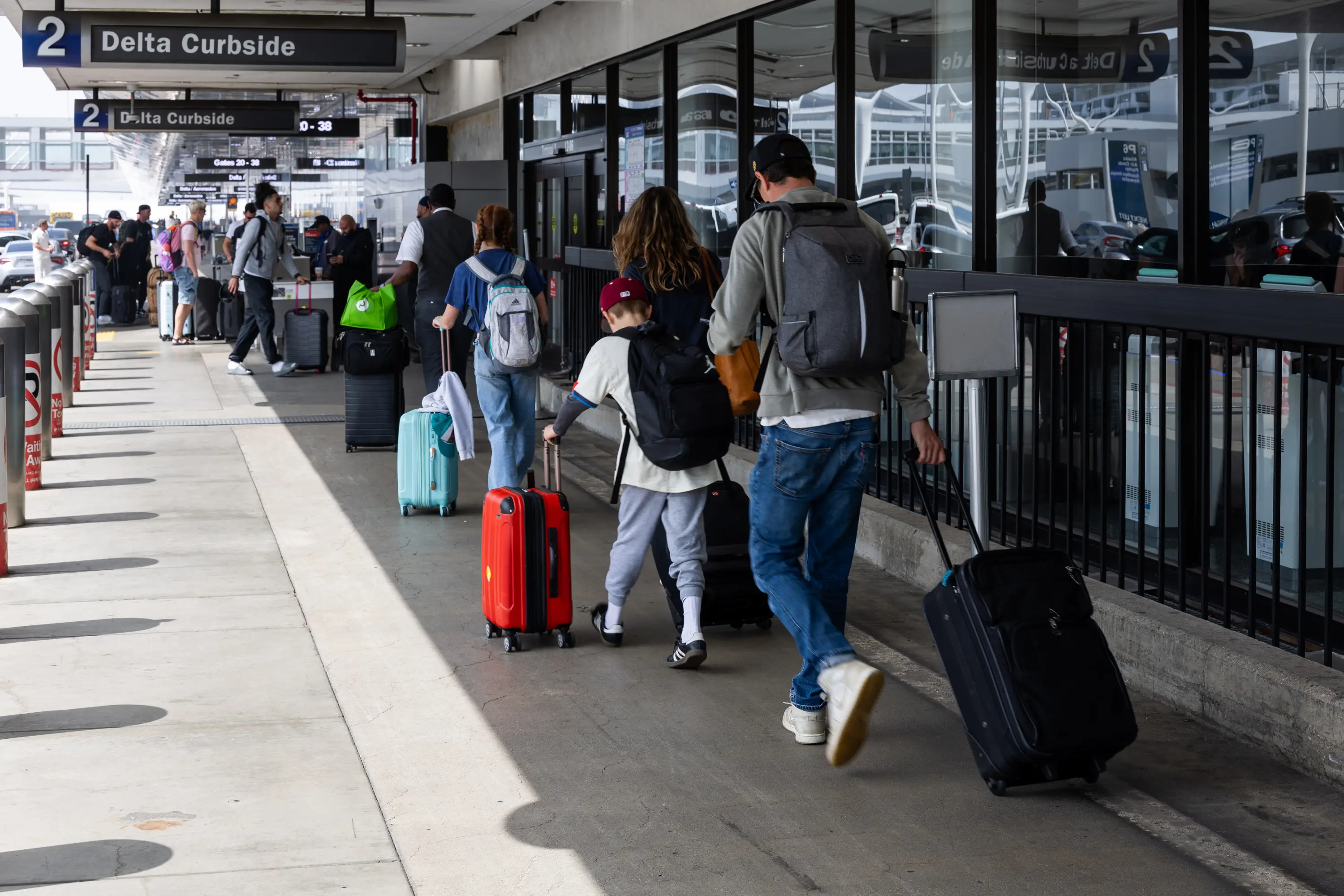Airport passengers walk while carrying suitcases on the Delta Air Lines curbside.
