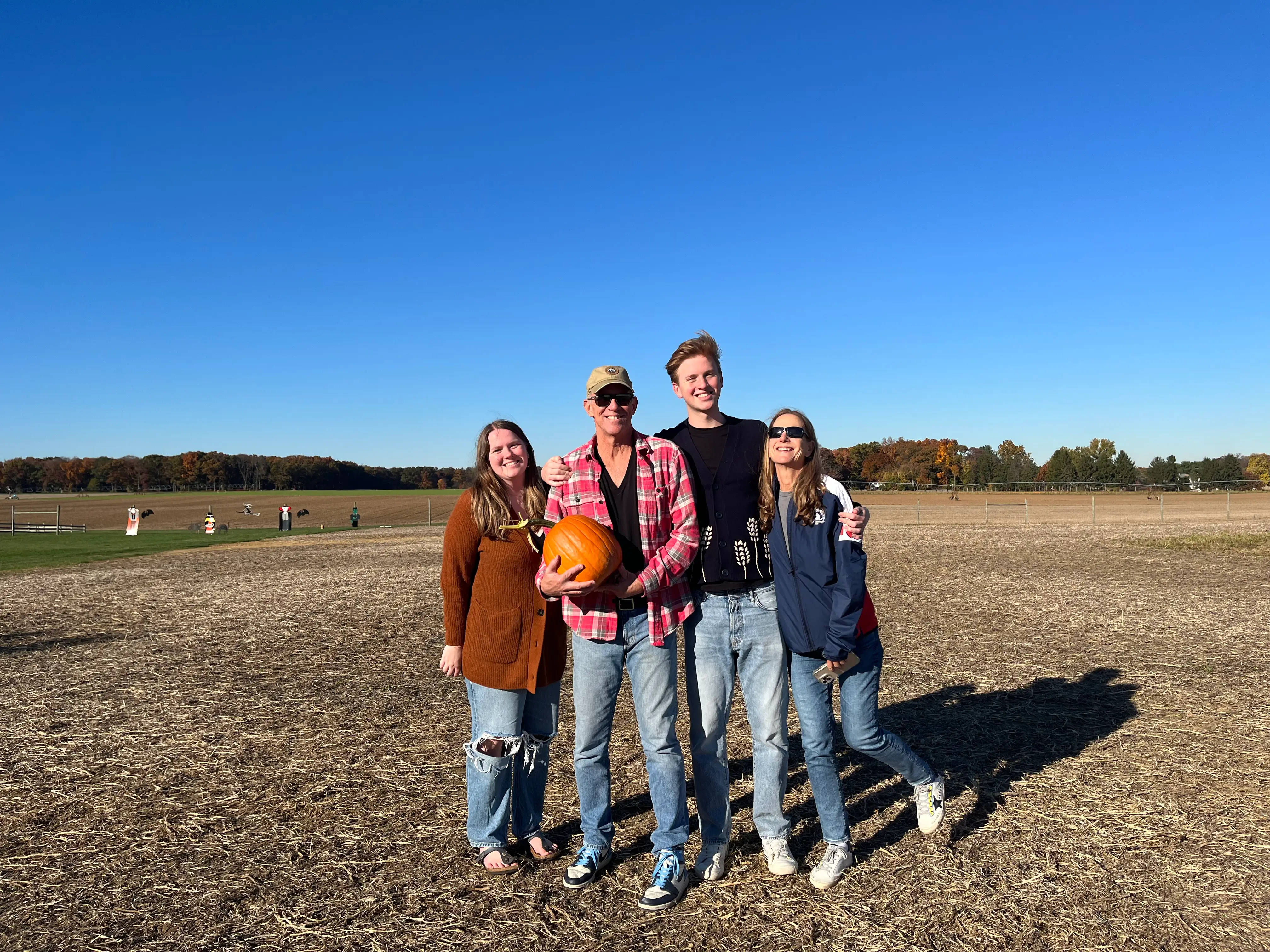 A family of four - mom, dad, son, and daughter - holds a pumpkin and smiles at the camera.