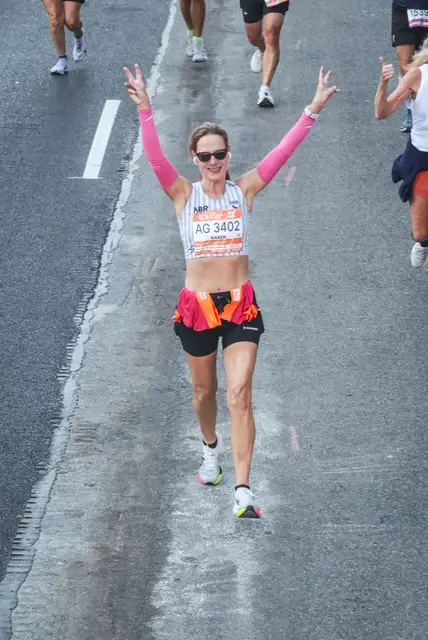 Karen Meadows has two peace signs in the air as she completes a marathon.