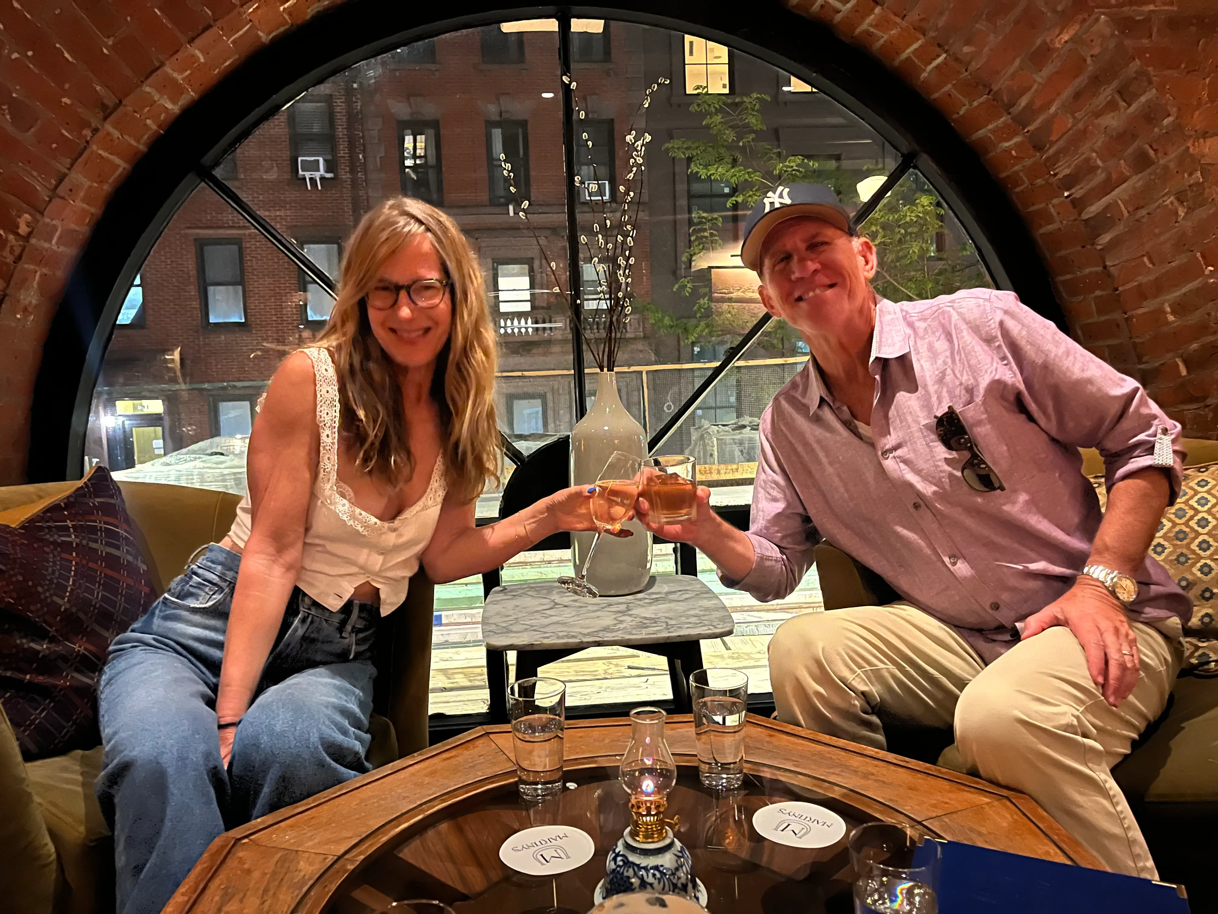 A woman and a man clink glasses at a restaurant and pose for a selfie.
