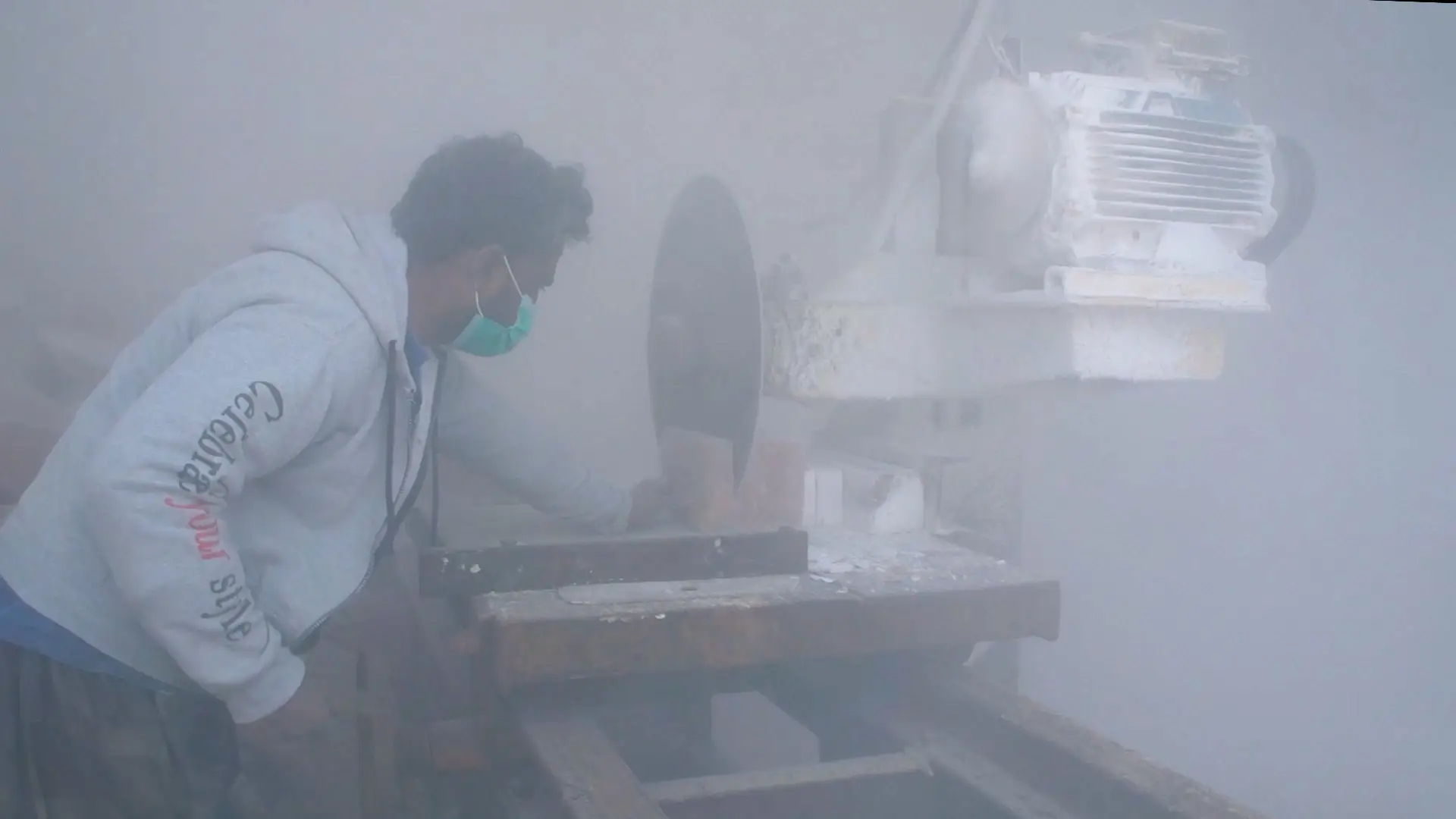 A man cutting a pink salt block surrounded by debris and dust in the air.