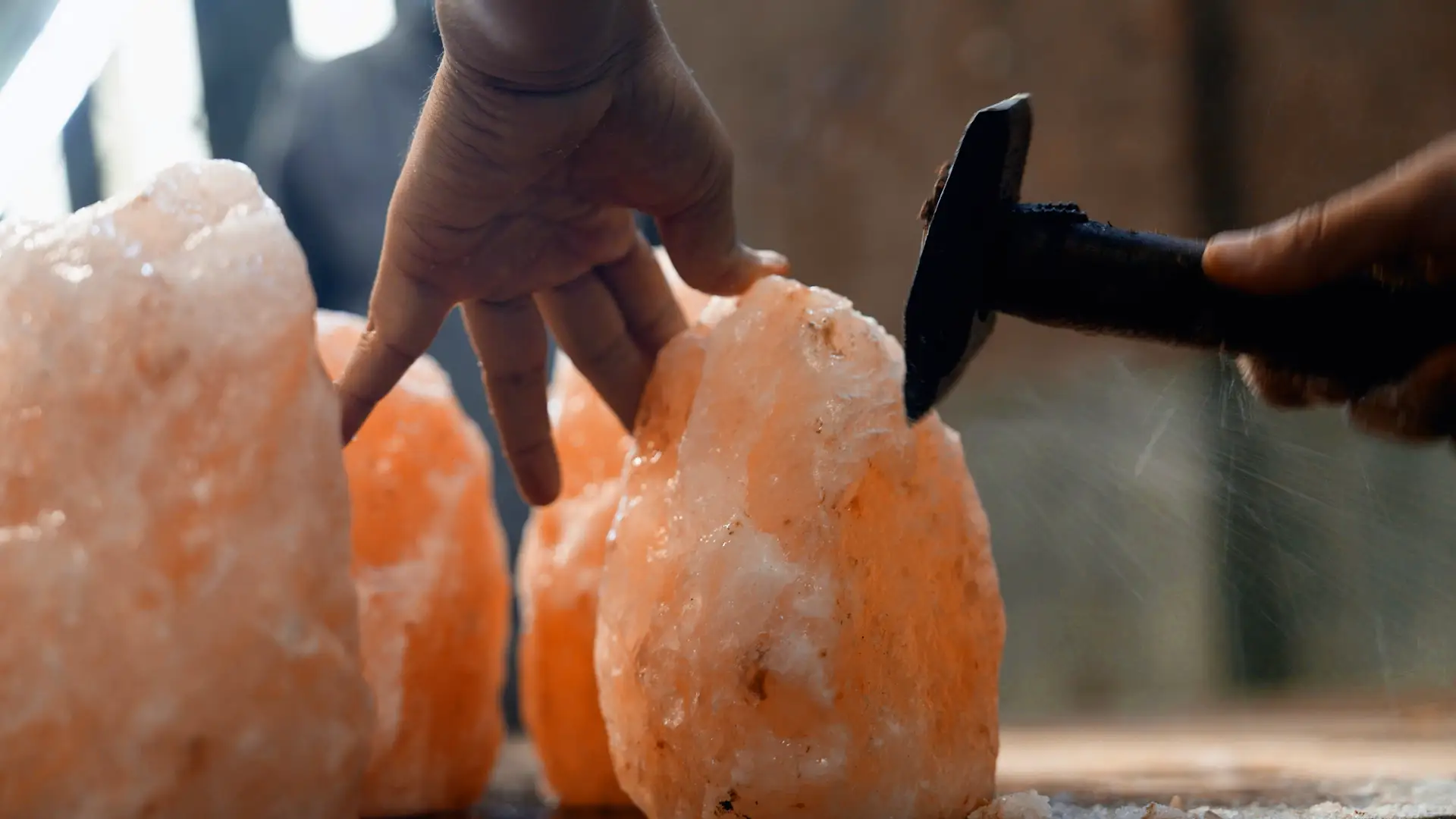 A person chisels down a piece of pink salt rock.