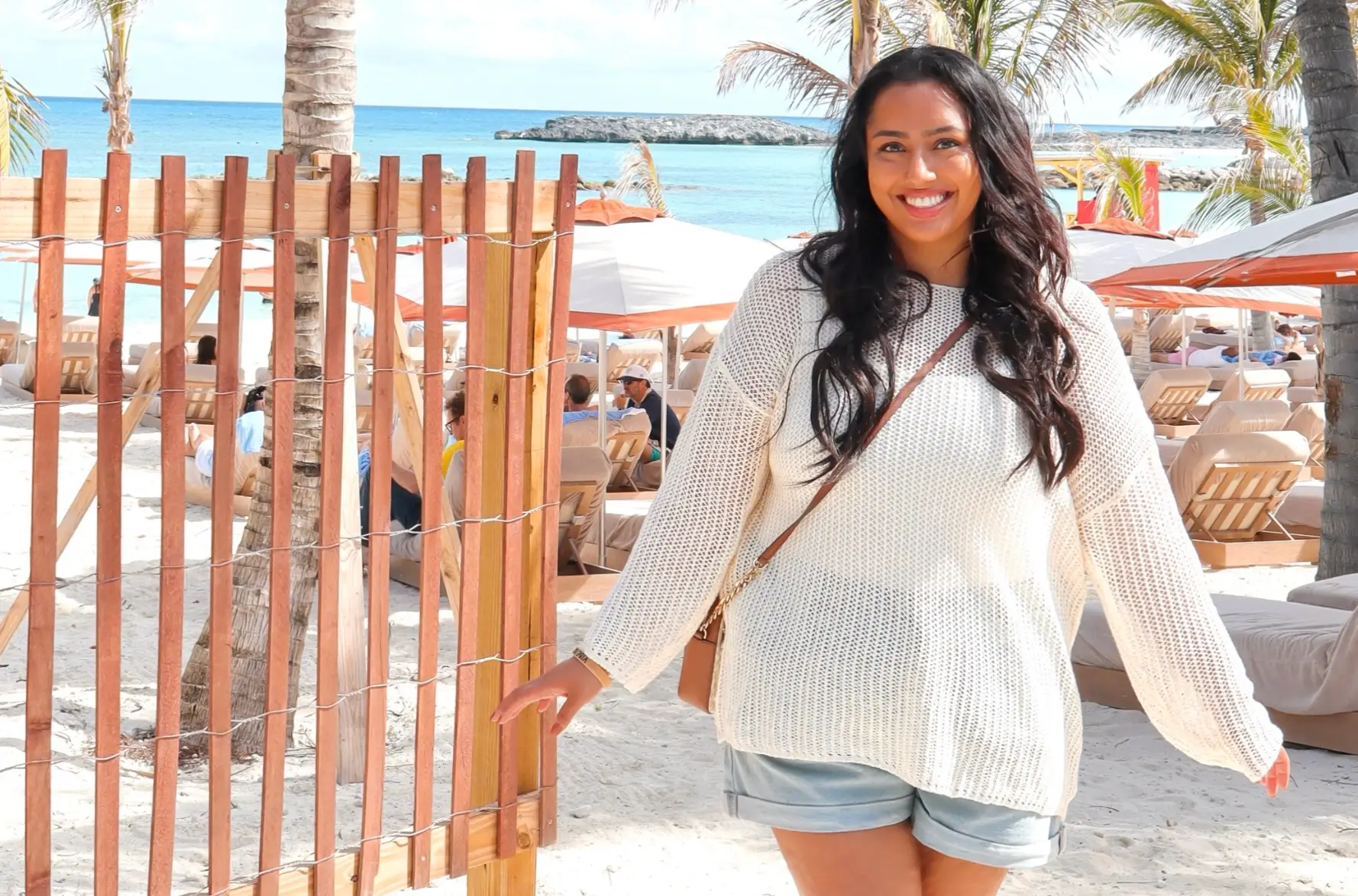 The writer standing in a sweater and shorts on the beach.