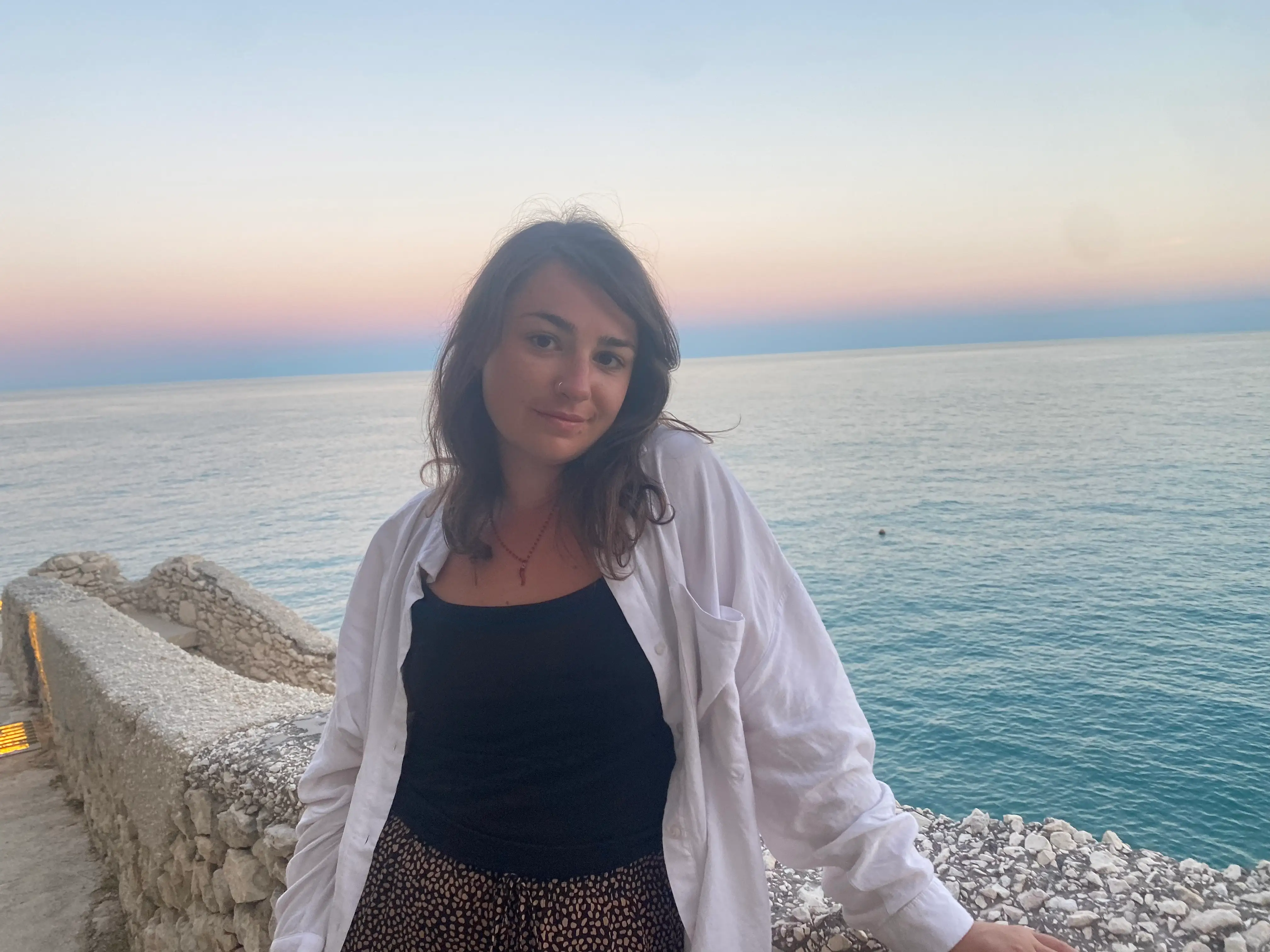 A woman posing with a sunset in Vieste, Italy in the background.