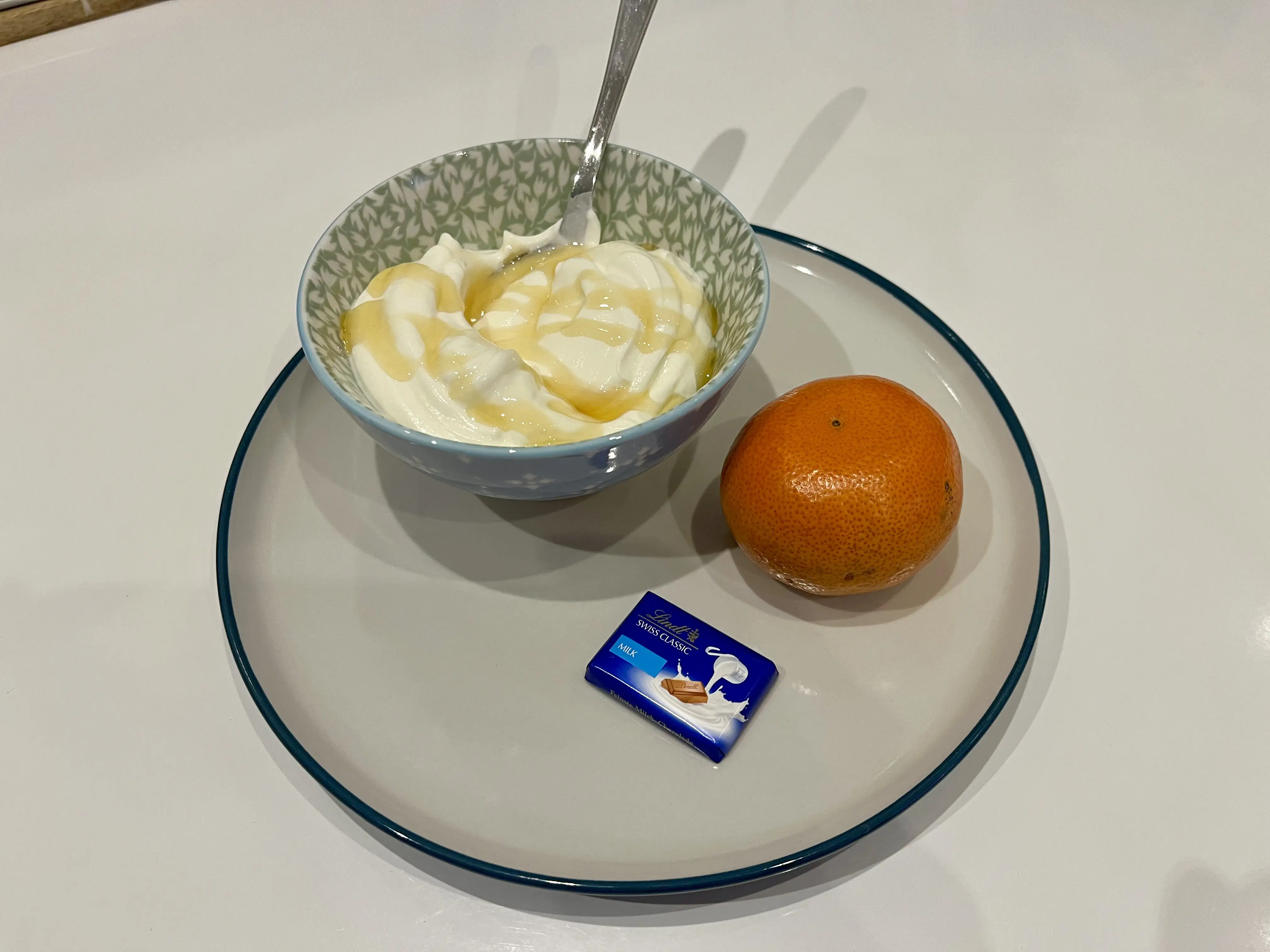 plate with yogurt and honey, a square of chocolate, and an orange