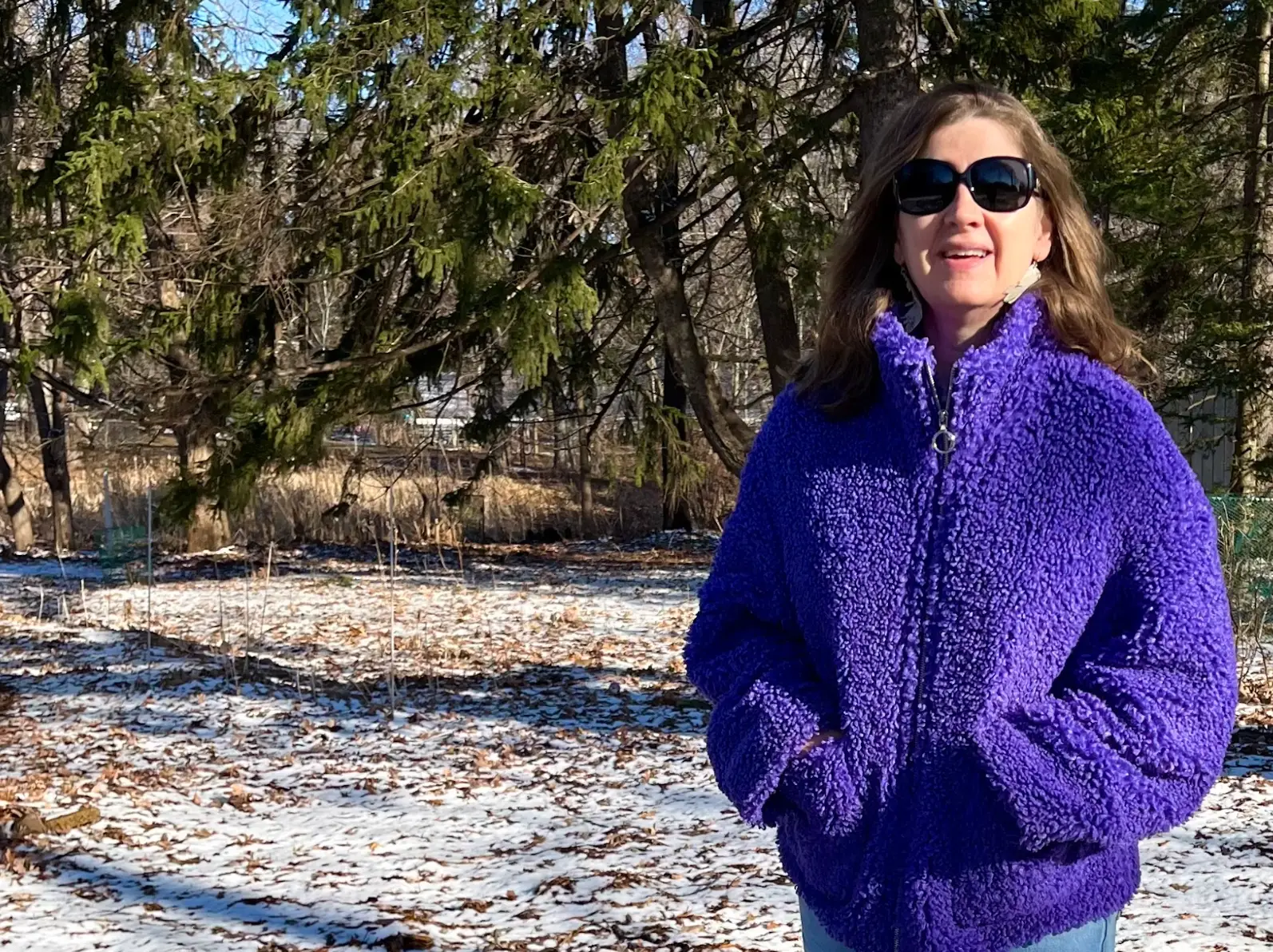 The writer standing in a purple sweater, in front of a snowy, woodsy background.