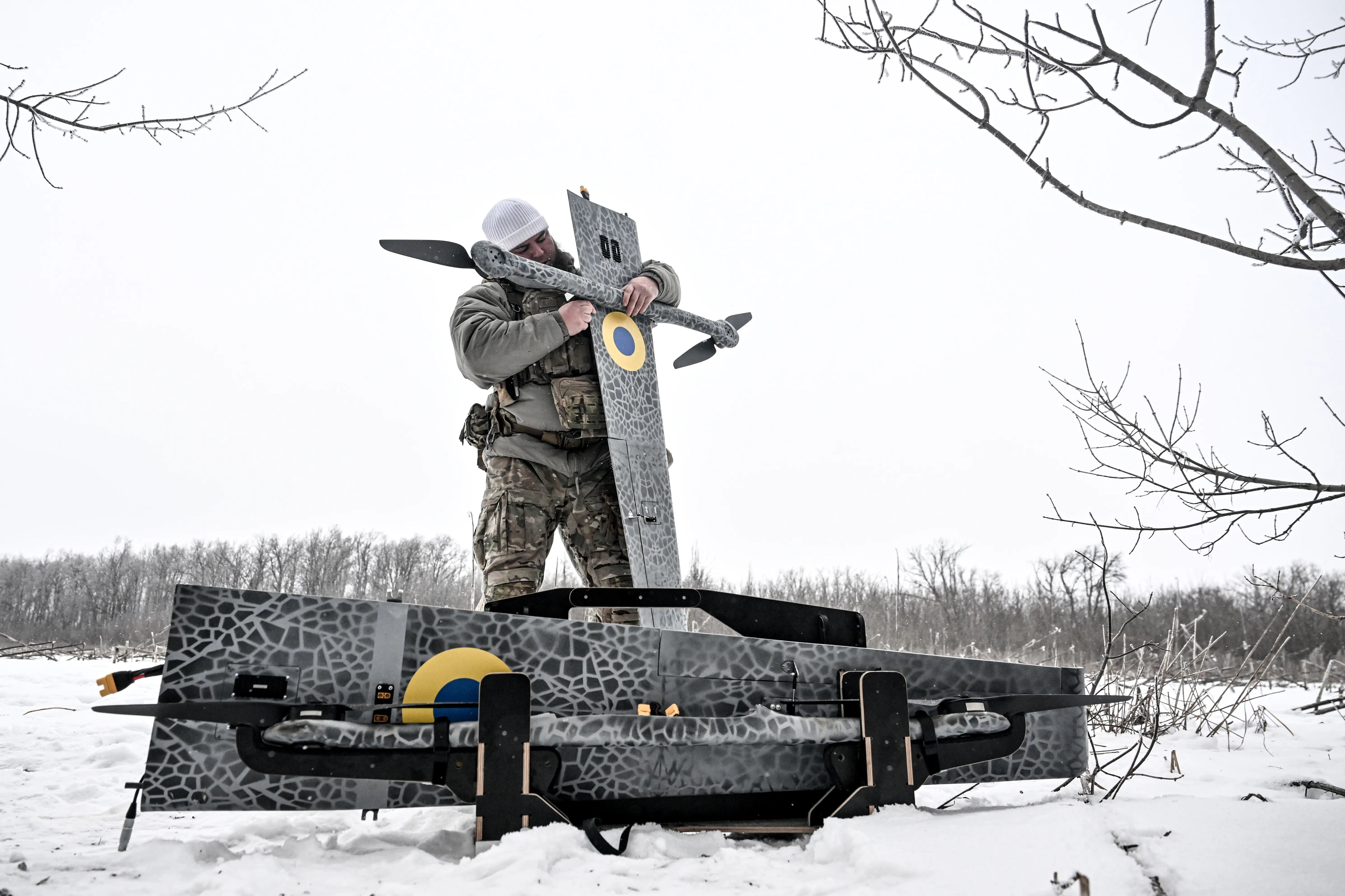 A man holds a grey drone vertical surrounded by snow