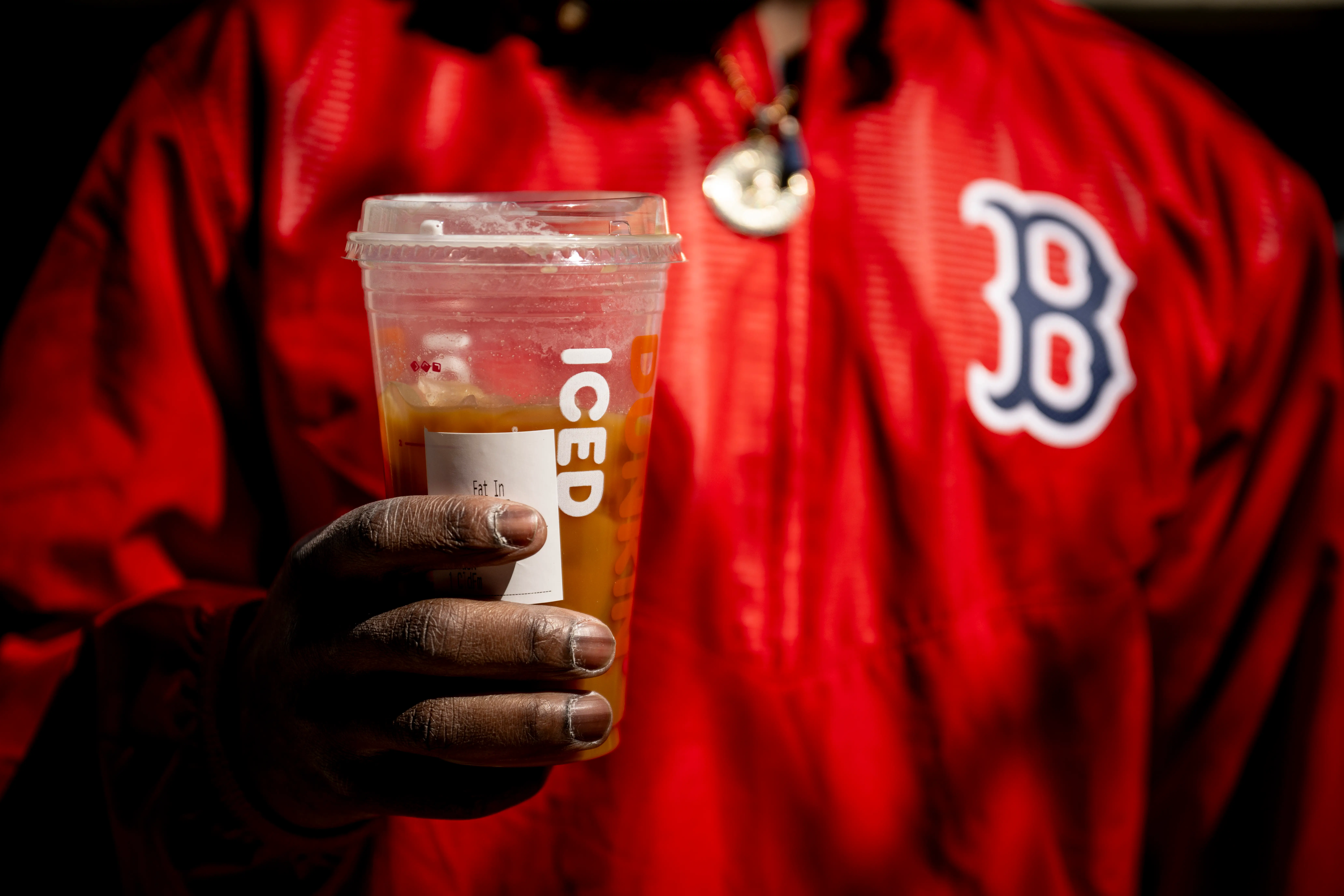 A Boston Red Sox Fan holds an iced Dunkin' coffee in their right hand.