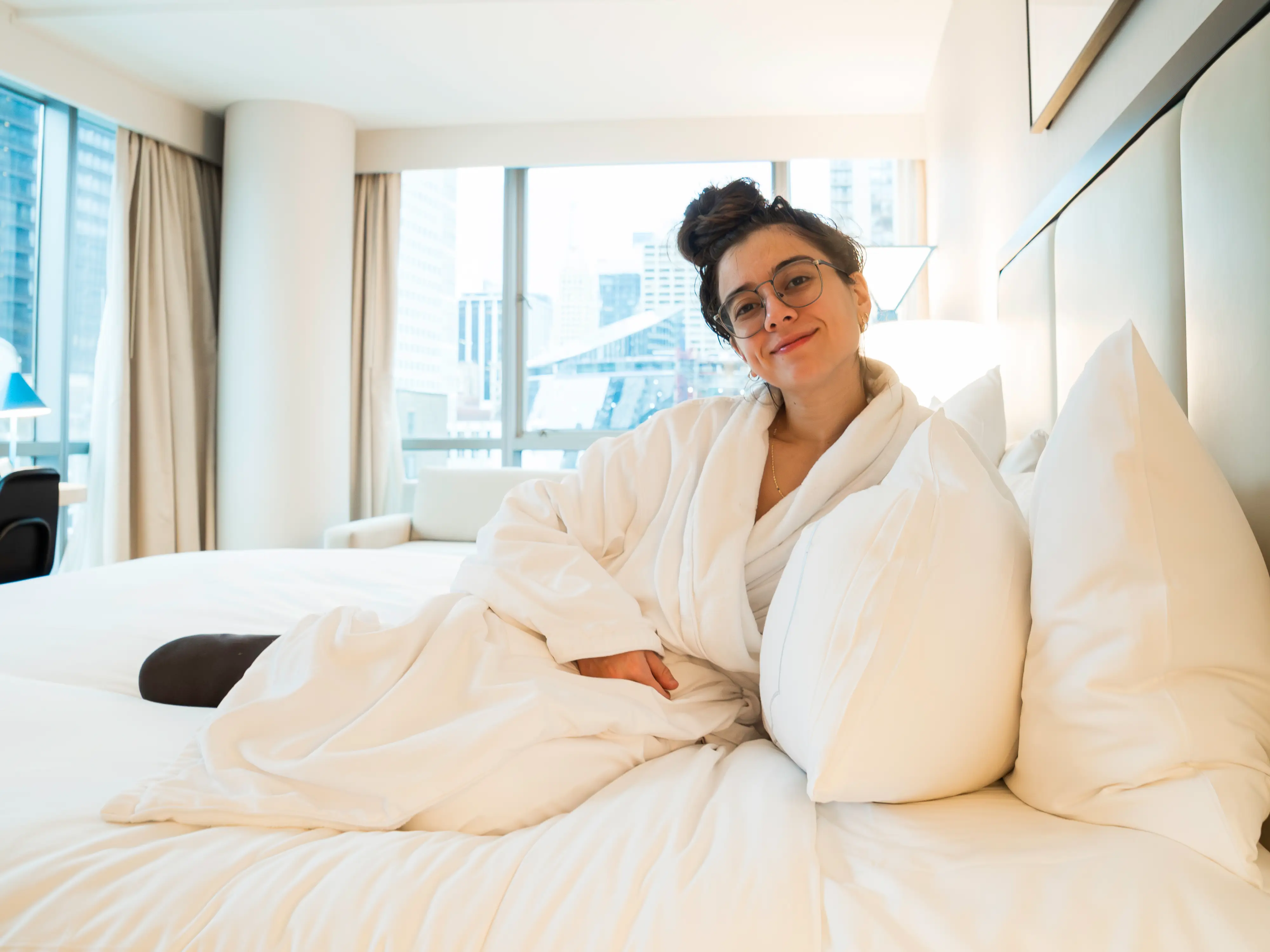 The author sitting in a robe on a bed in her room at the Wit hotel with floor-to-ceiling windows in the background