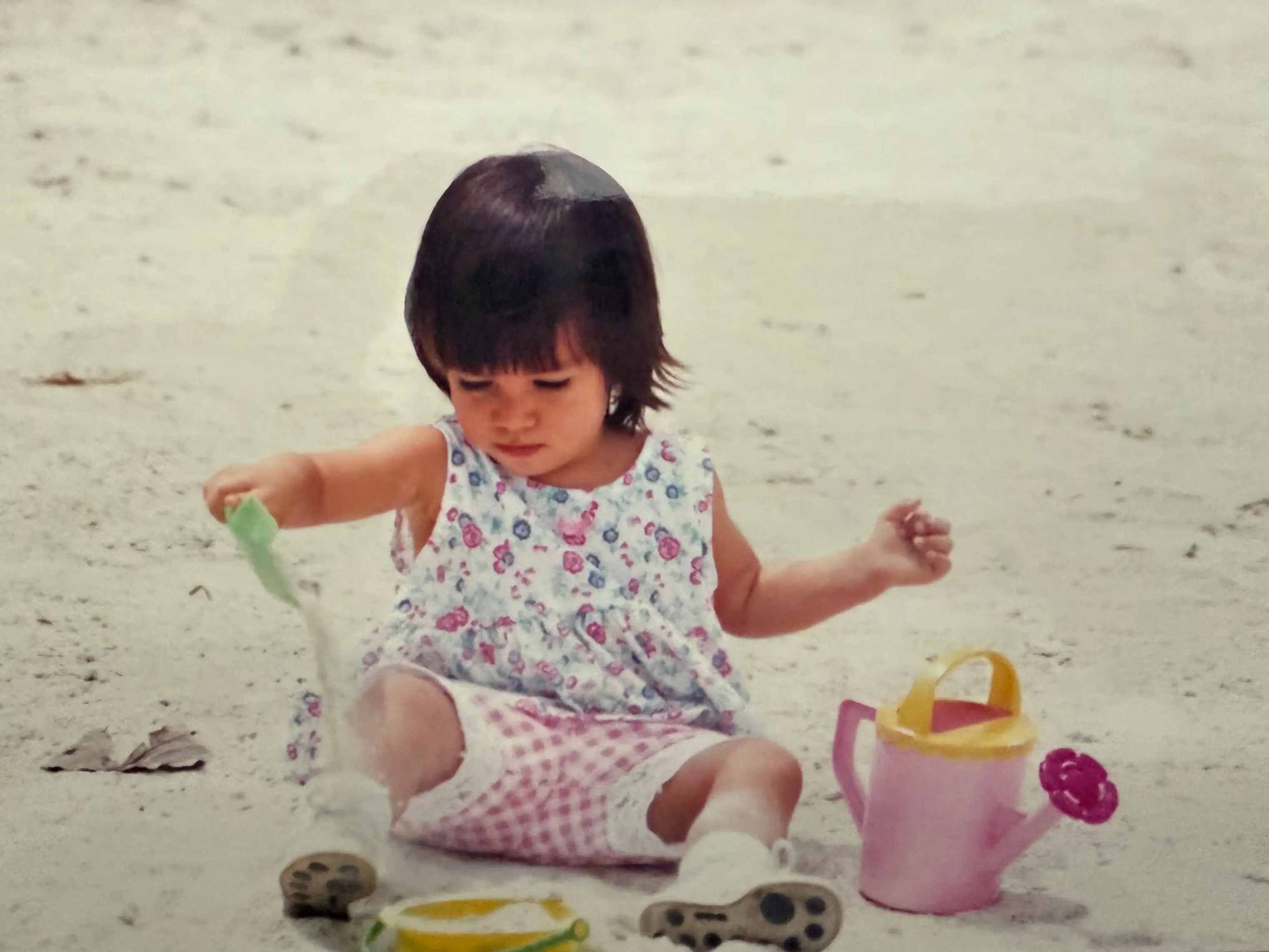 A picture of a baby girl playing with a toy shovel in the sand.