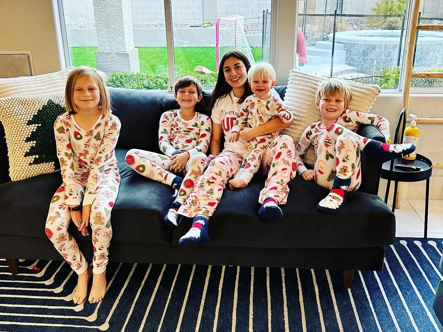 Three children and a young woman in Christmas-themed pajamas.