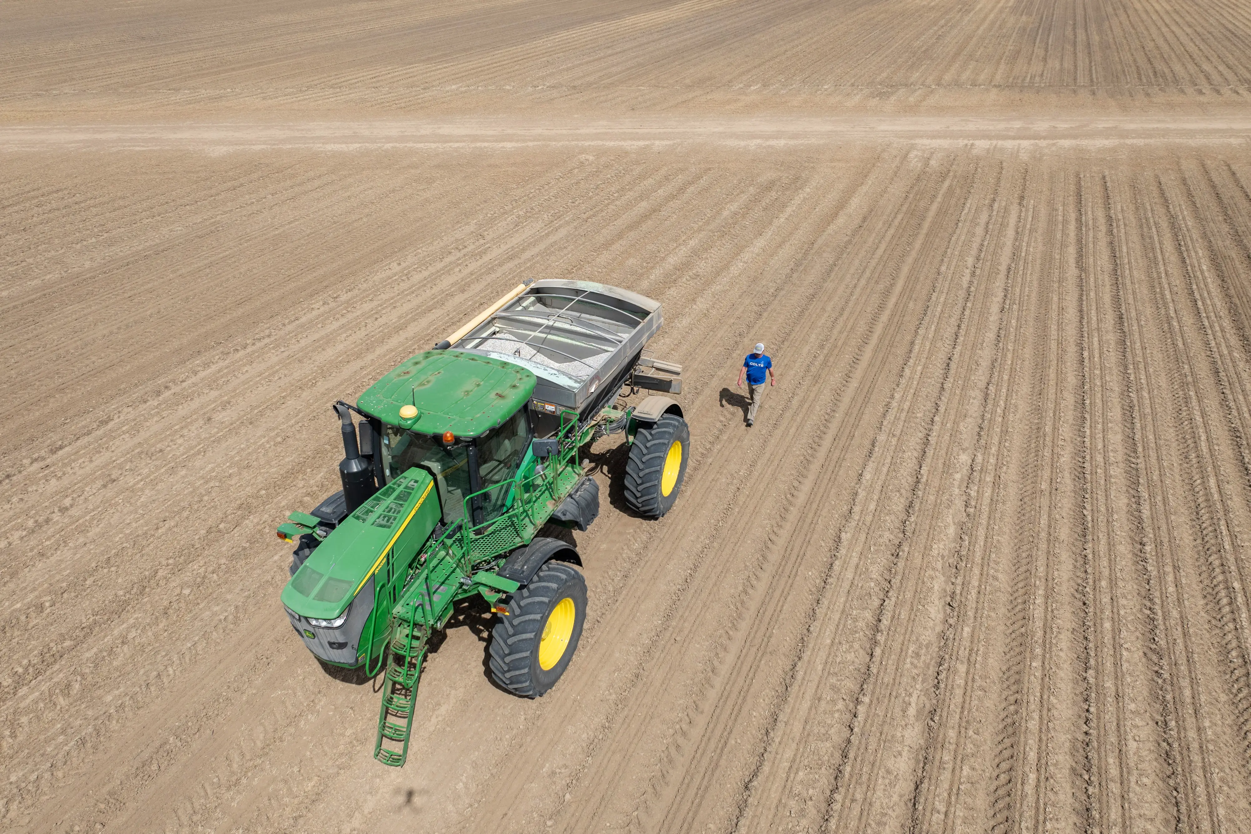 A man walks next to a large farming vehicle in a field.