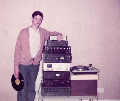 A young man holding a record next to a record player soundsystem.
