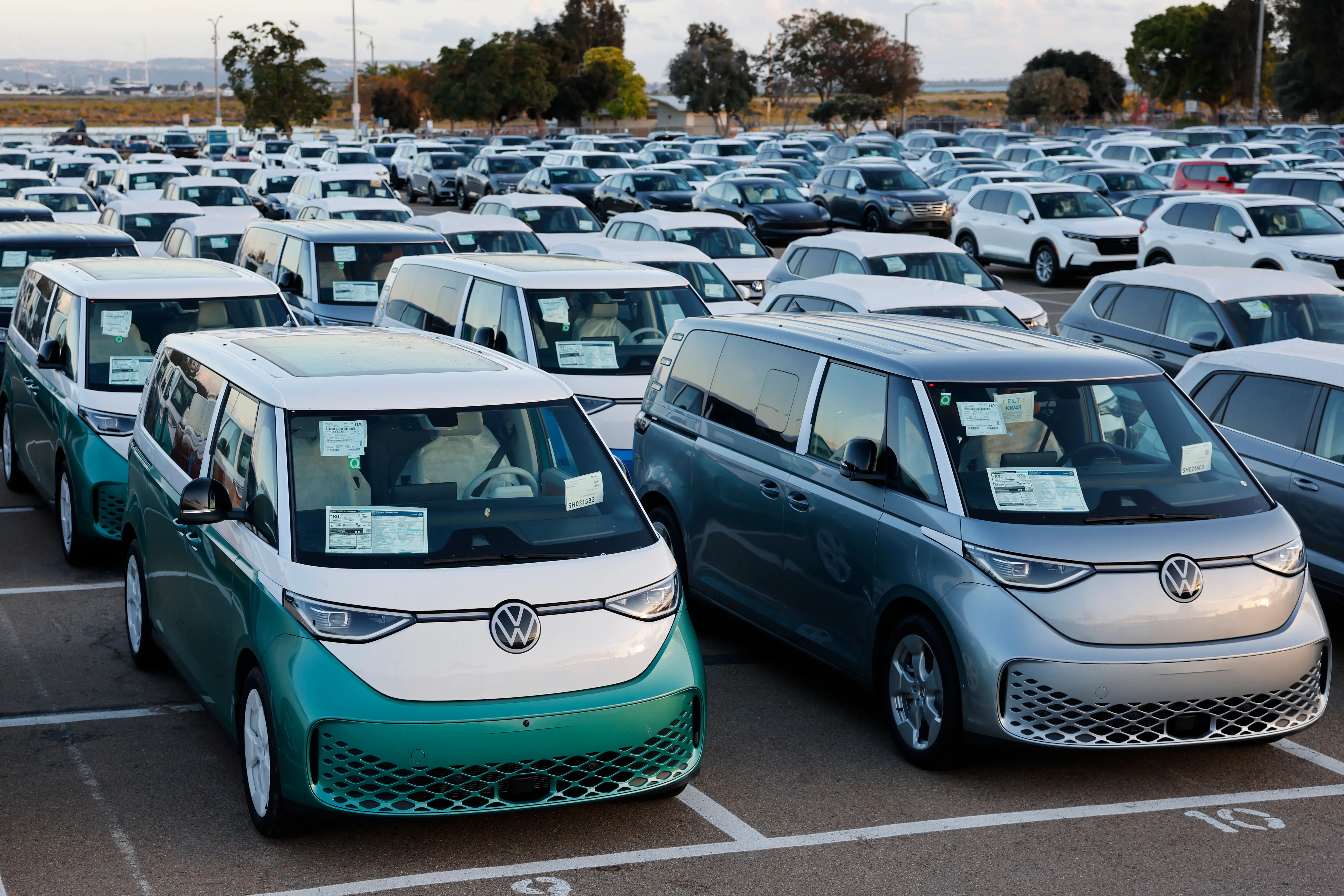 A row of Volkswagen ID. Buzz vans are parked in a large car holding area.