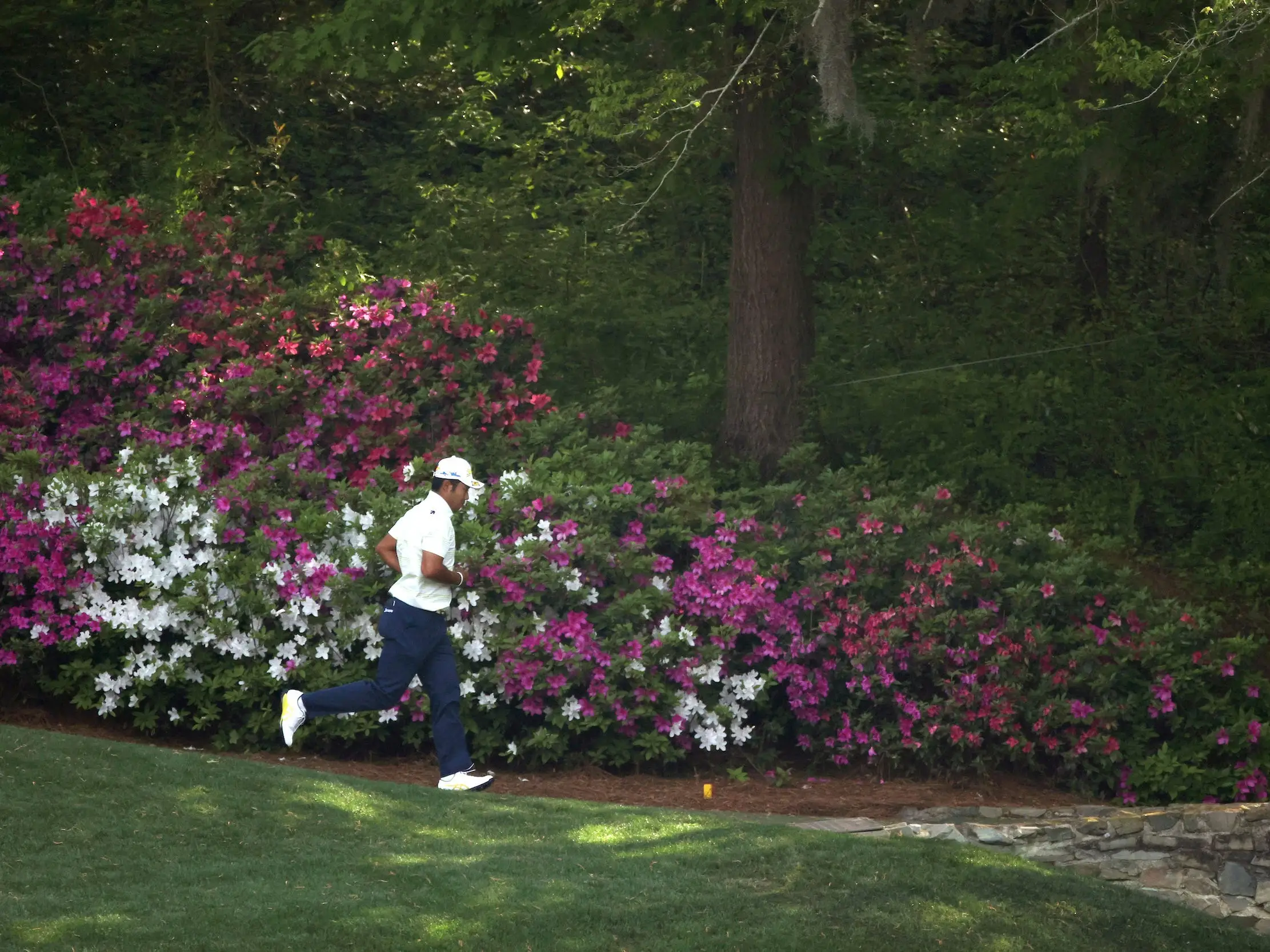 Hideki Matsuyama runs past the azaleas at the Masters.