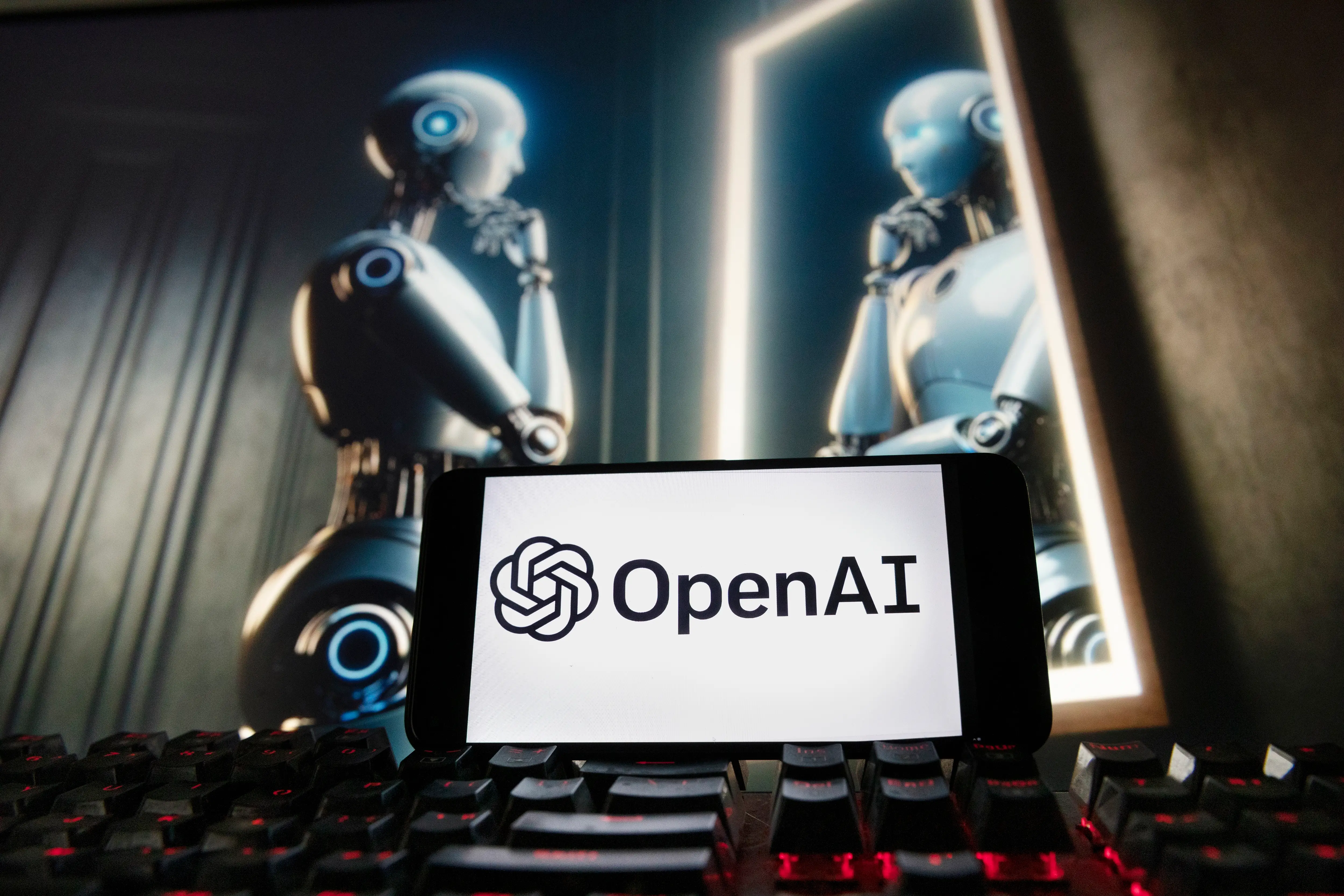 The OpenAI logo is displayed on a cellphone with an image on a computer monitor generated by ChatGPT's Dall-E text-to-image model in 2023 in Boston