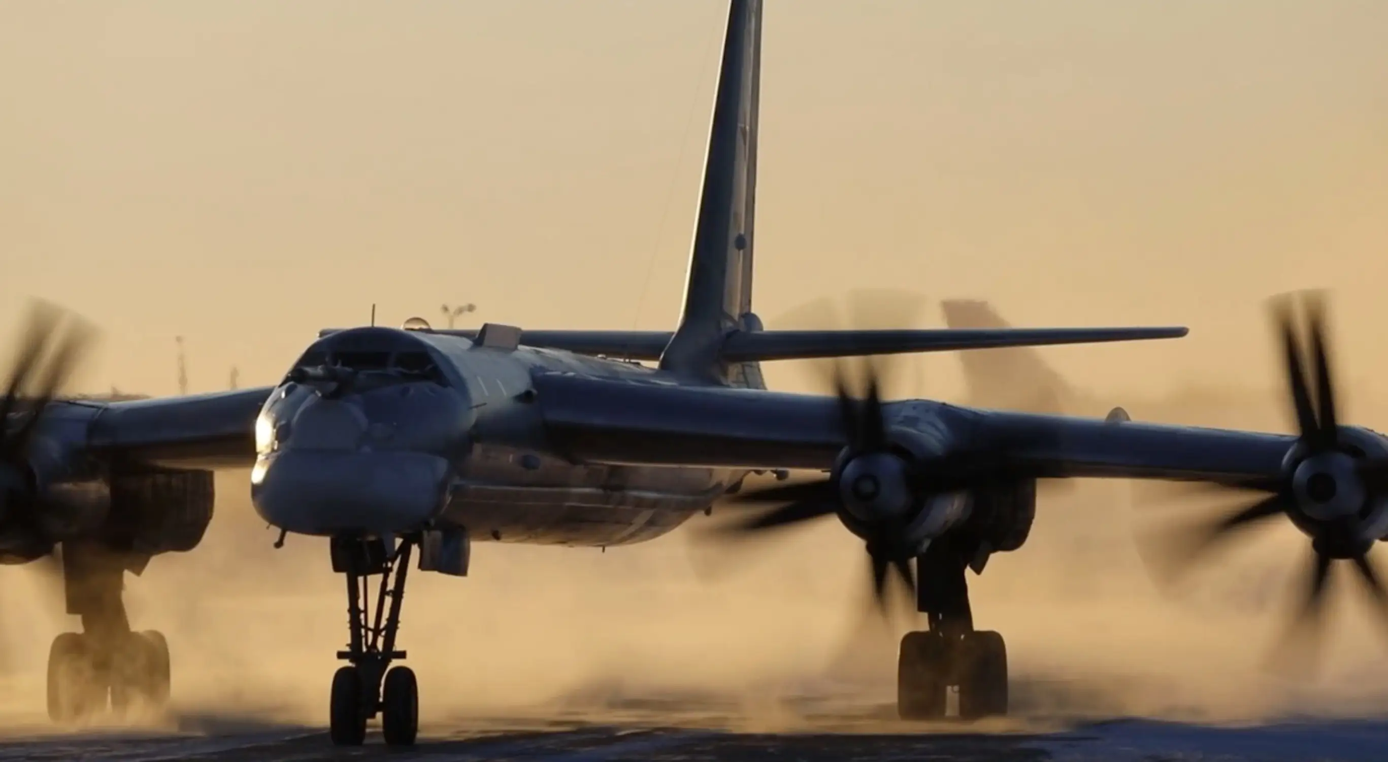 A dark and shiny looking aircraft sihouetted in an orange sky with spilling propellers on tarmac