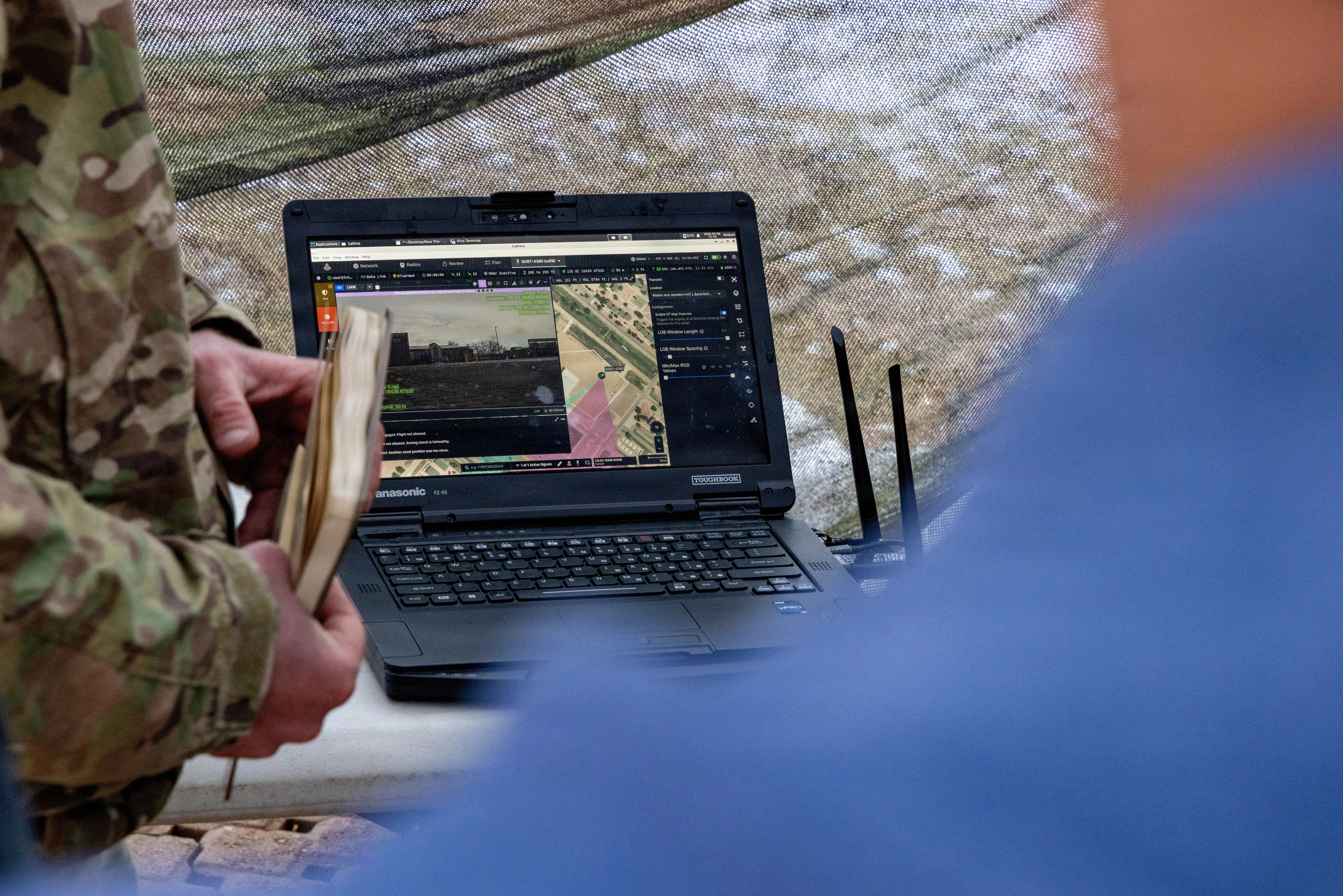 A laptop computer sits at a desk with people standing around it.