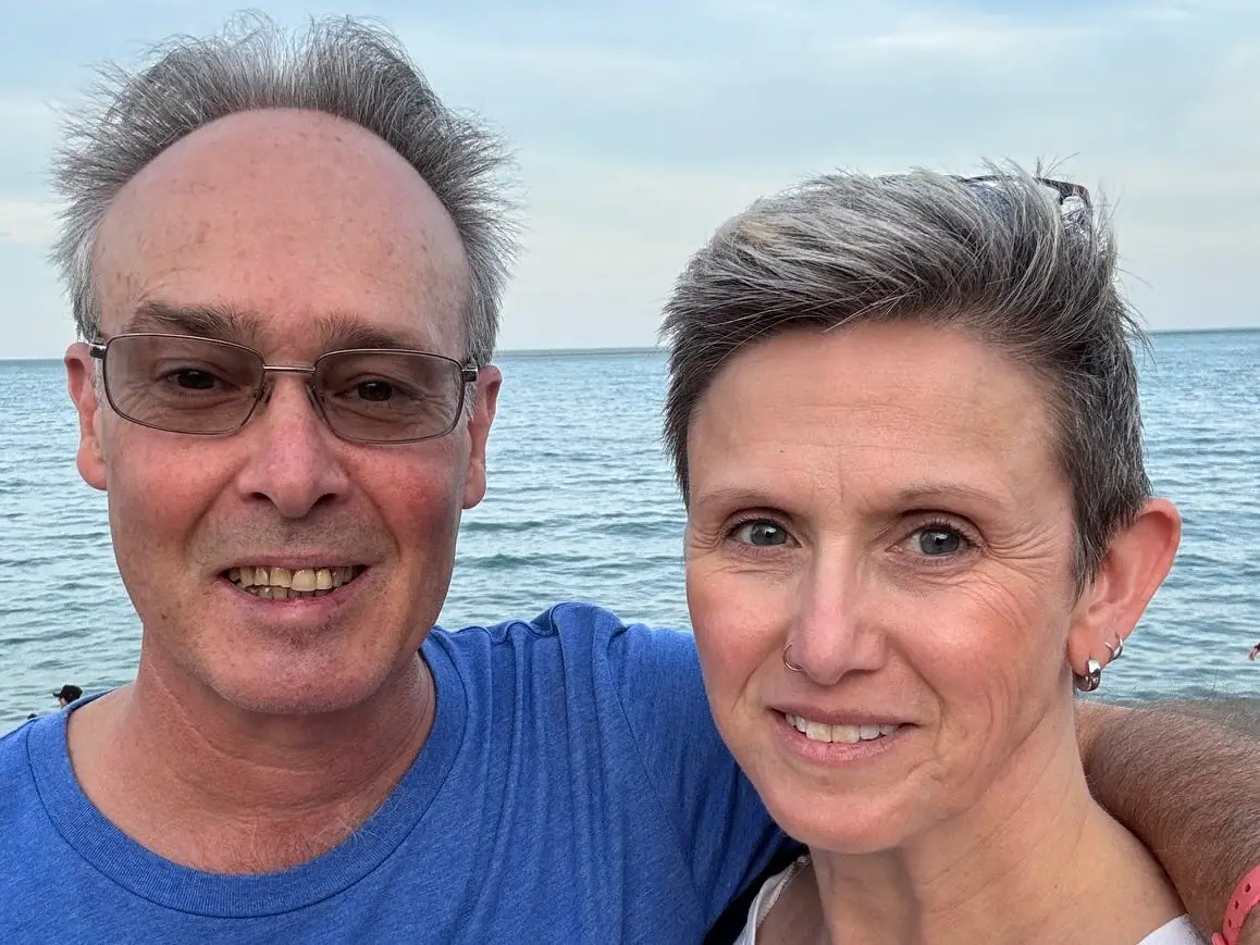 A man and woman on vacation standing in front of the ocean.