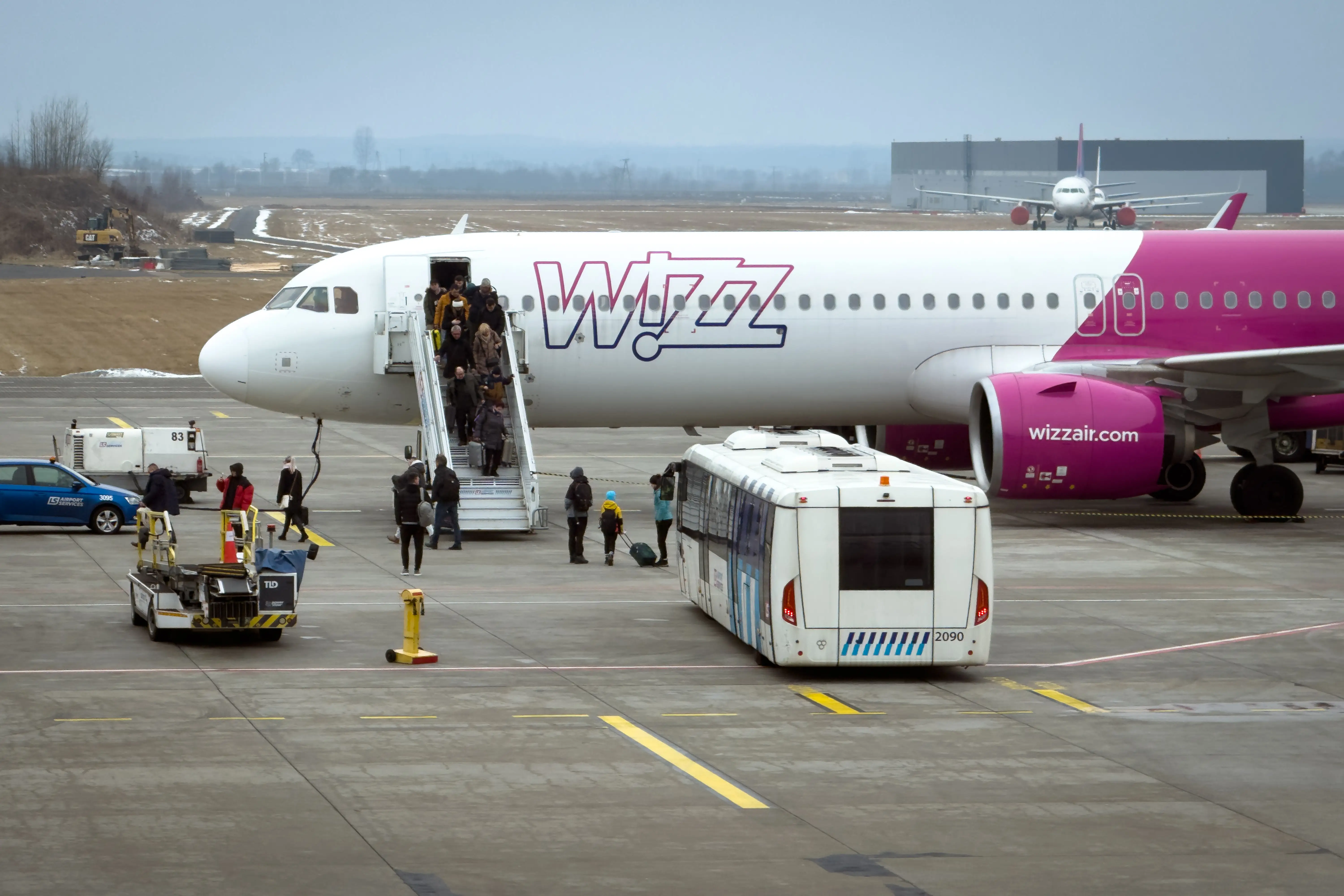 A Wizz Air Malta Airbus A321neo, registration 9H-WBF, stands on the apron while arriving passengers disembark and walk across the apron toward Terminal C at Katowice Airport in Pyrzowice, on February 21, 2026.
