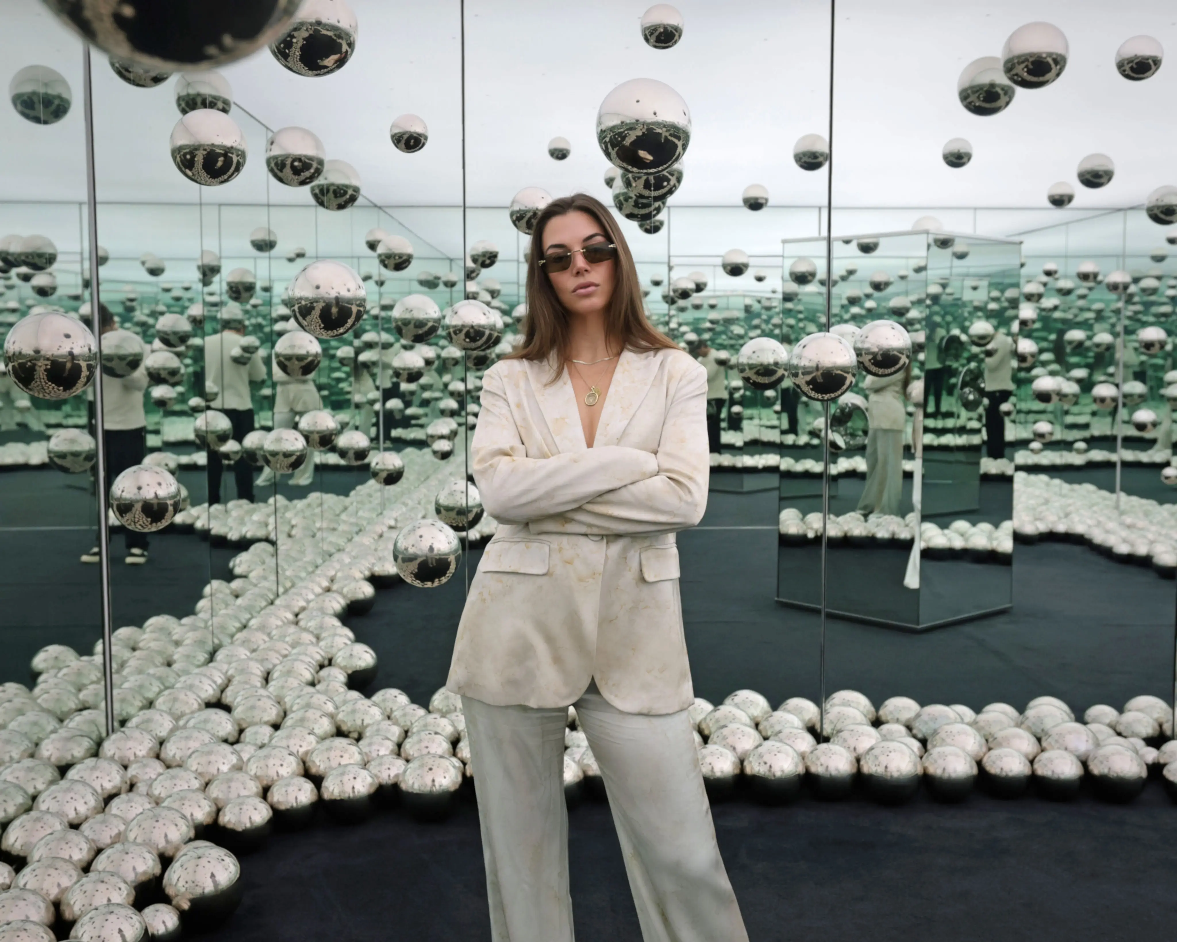 Taylor wears sunglasses and a white pantsuit in a mirrored room in the Rubell Museum.