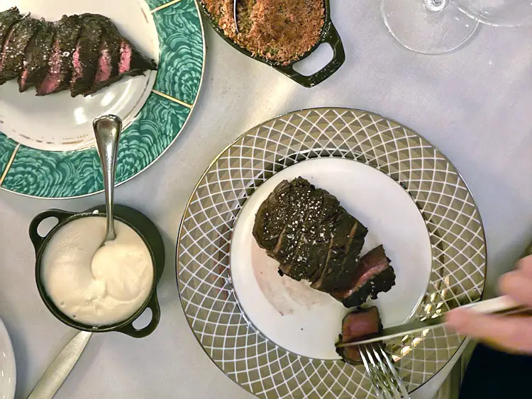 A table with plates of steak, a sauce, and a side dish.