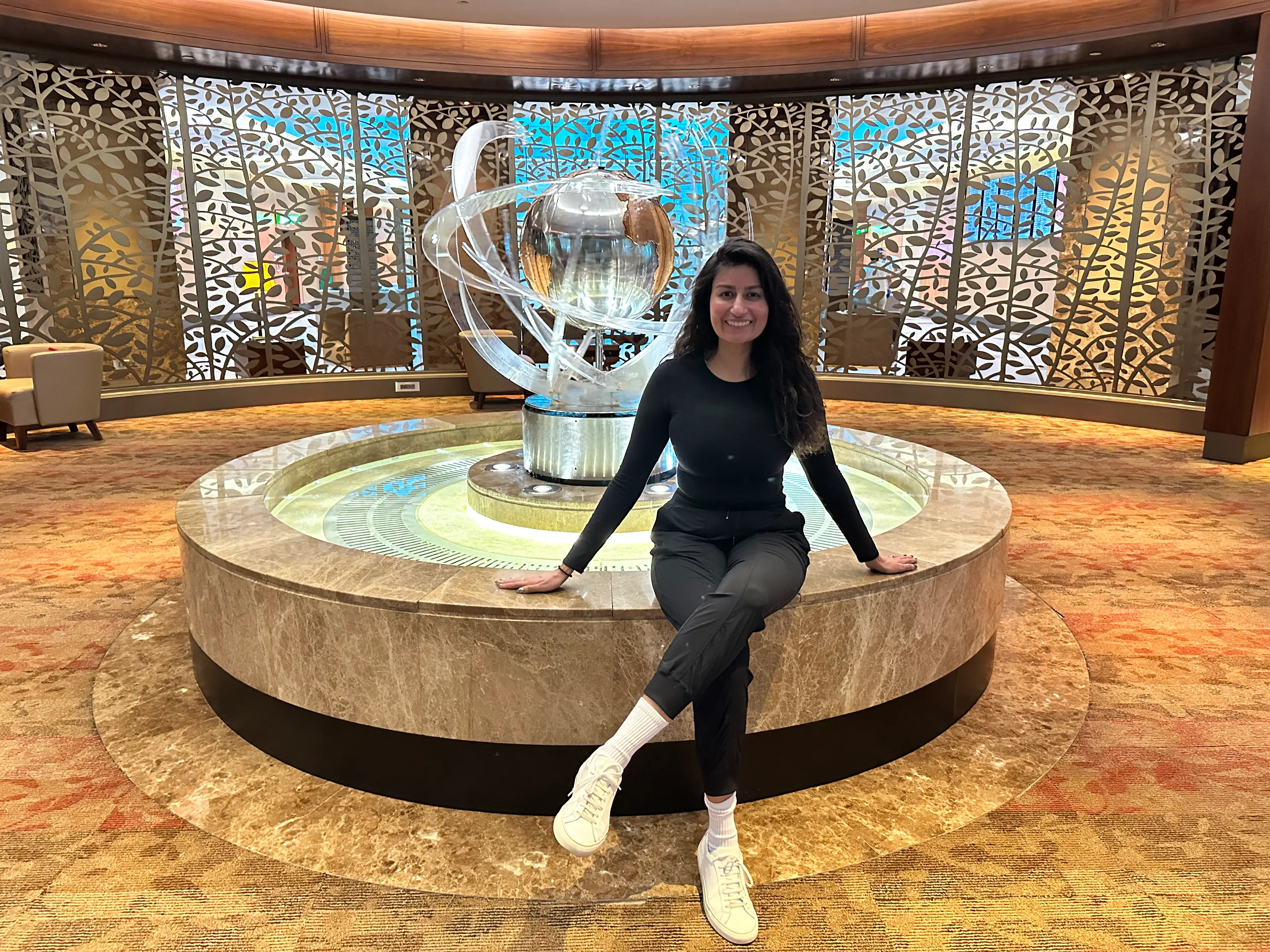 Alyssa sits on the edge of a fountain in a beautiful airport lounge.