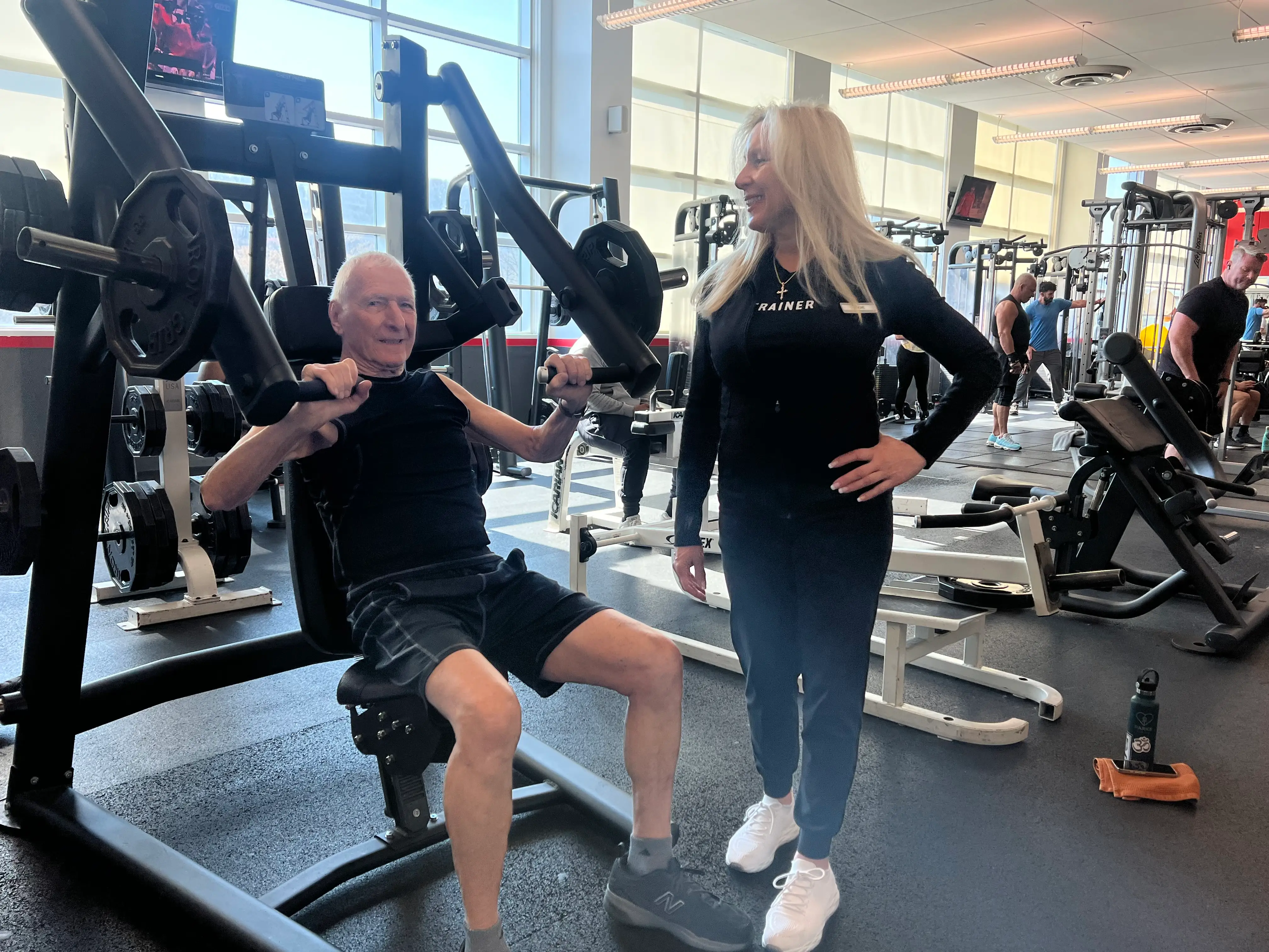 A senior lifting weights supervised by his personal trainer