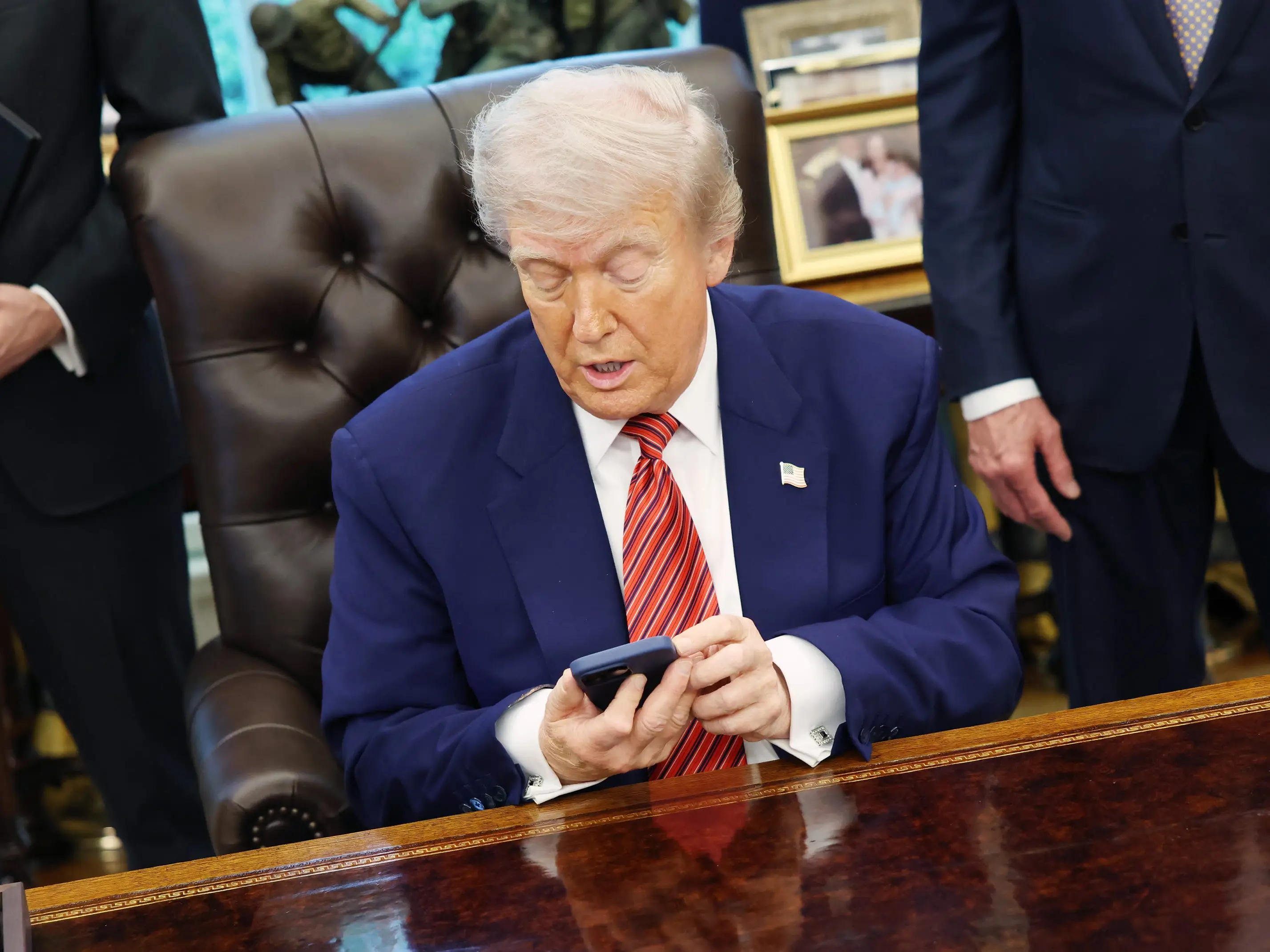 President Trump looks at his phone at the oval office desk.