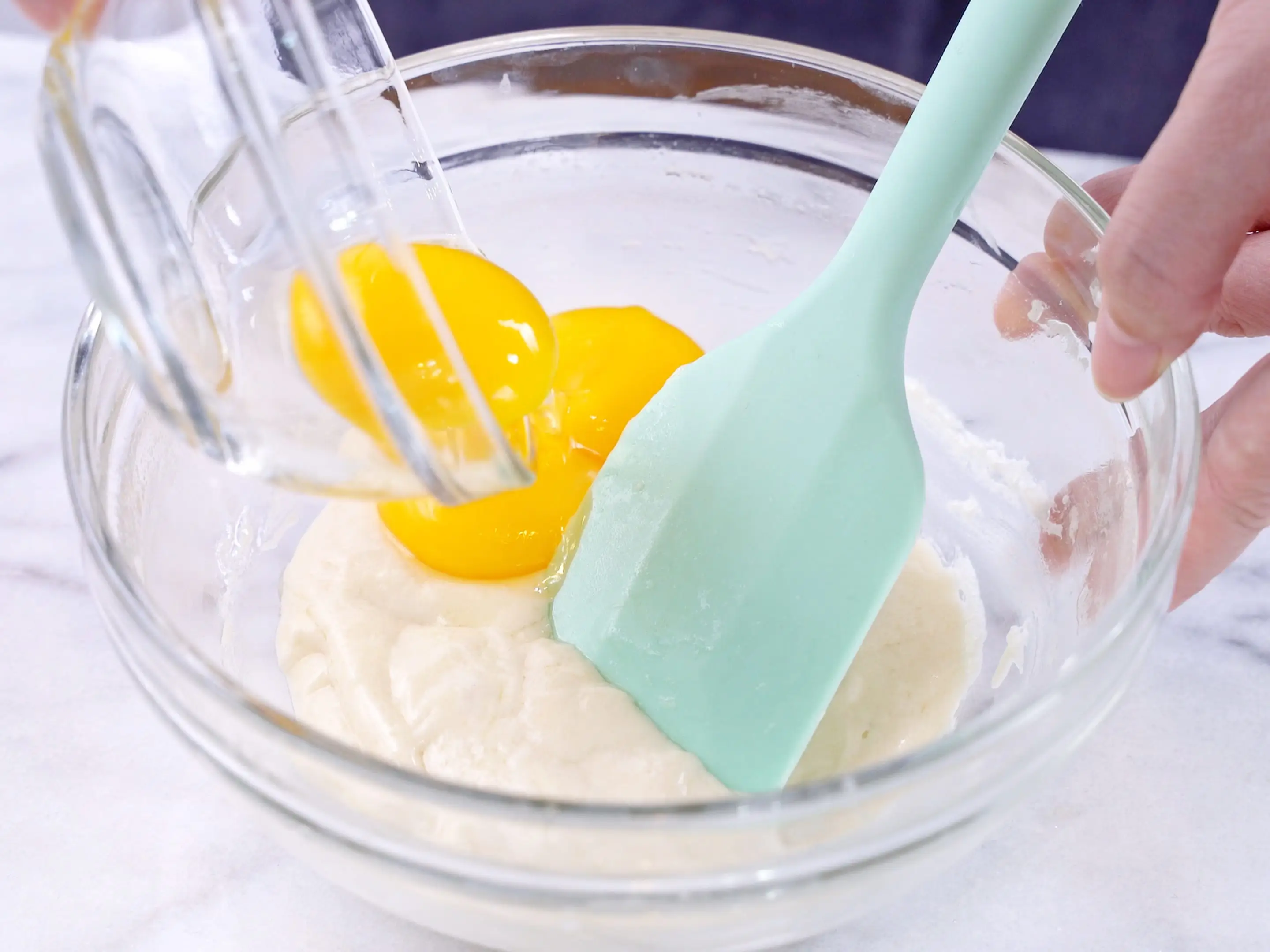 Mixing egg yolk into cake batter with rubber spatula mixer tool stirring
