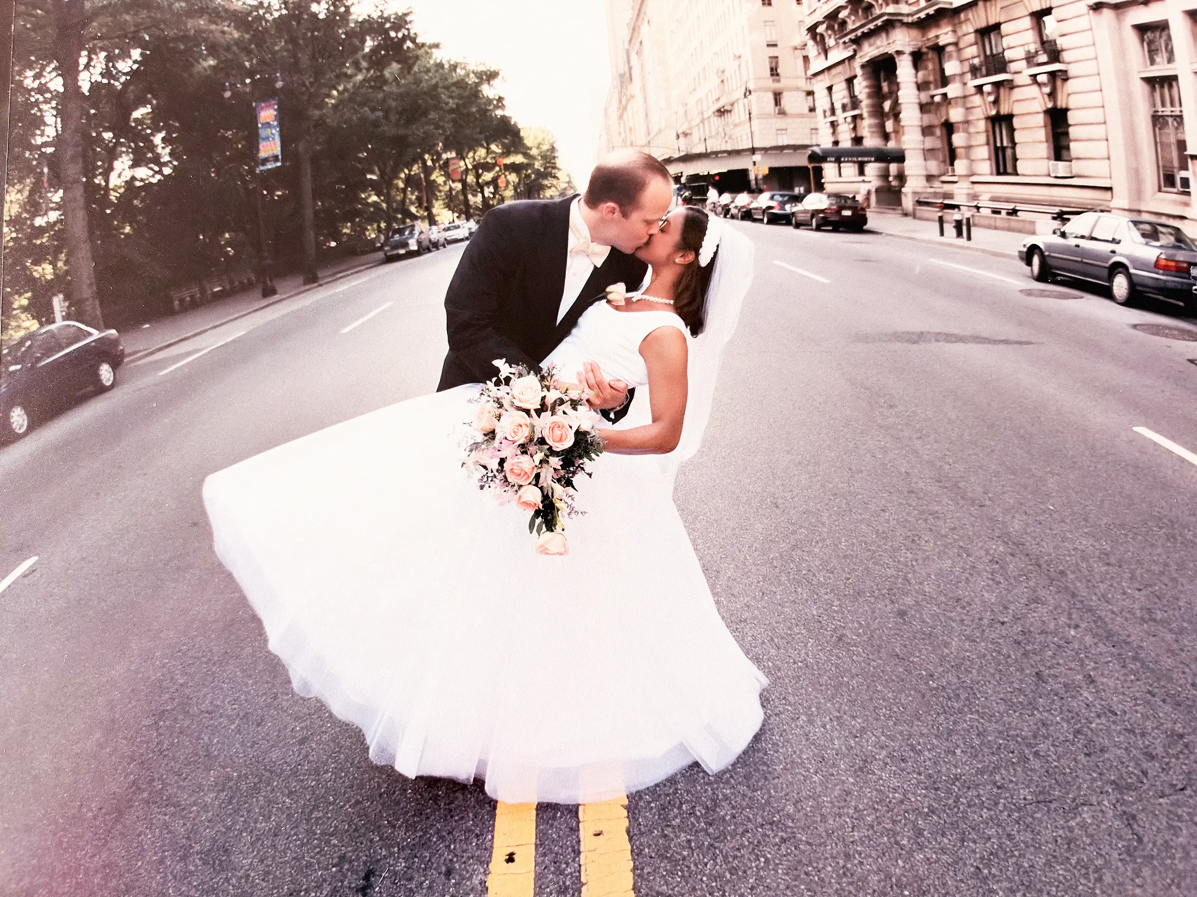 Susan Teresa in a wedding dress on her wedding day being kissed by the groom in the middle of the street