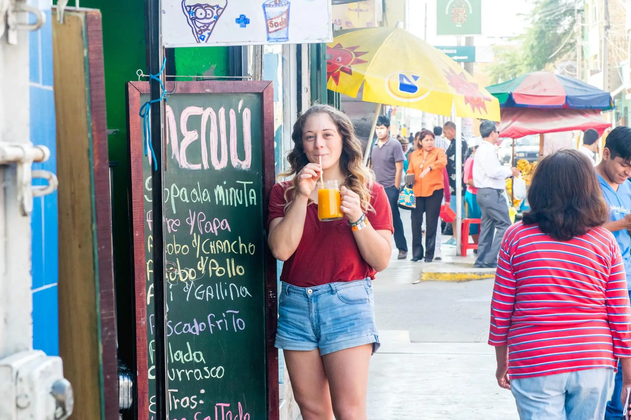 Author drinking orange beverage next to chalkboard sign