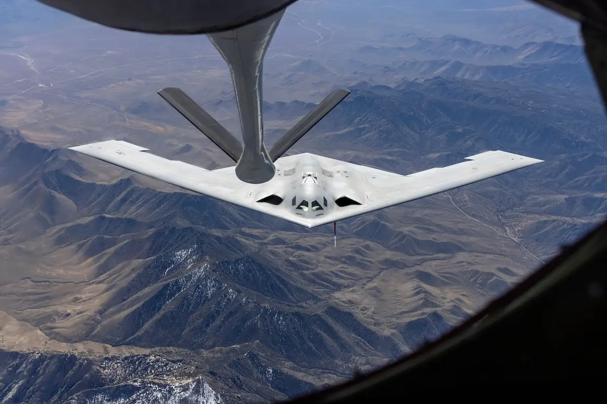 A B-21 Raider bomber flies above mountains.