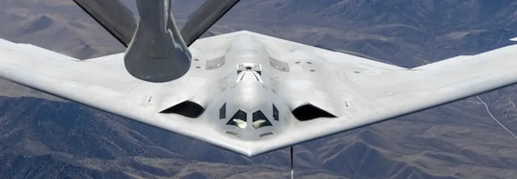 A US Air Force B-21 Raider bomber flies over mountainous terrain.