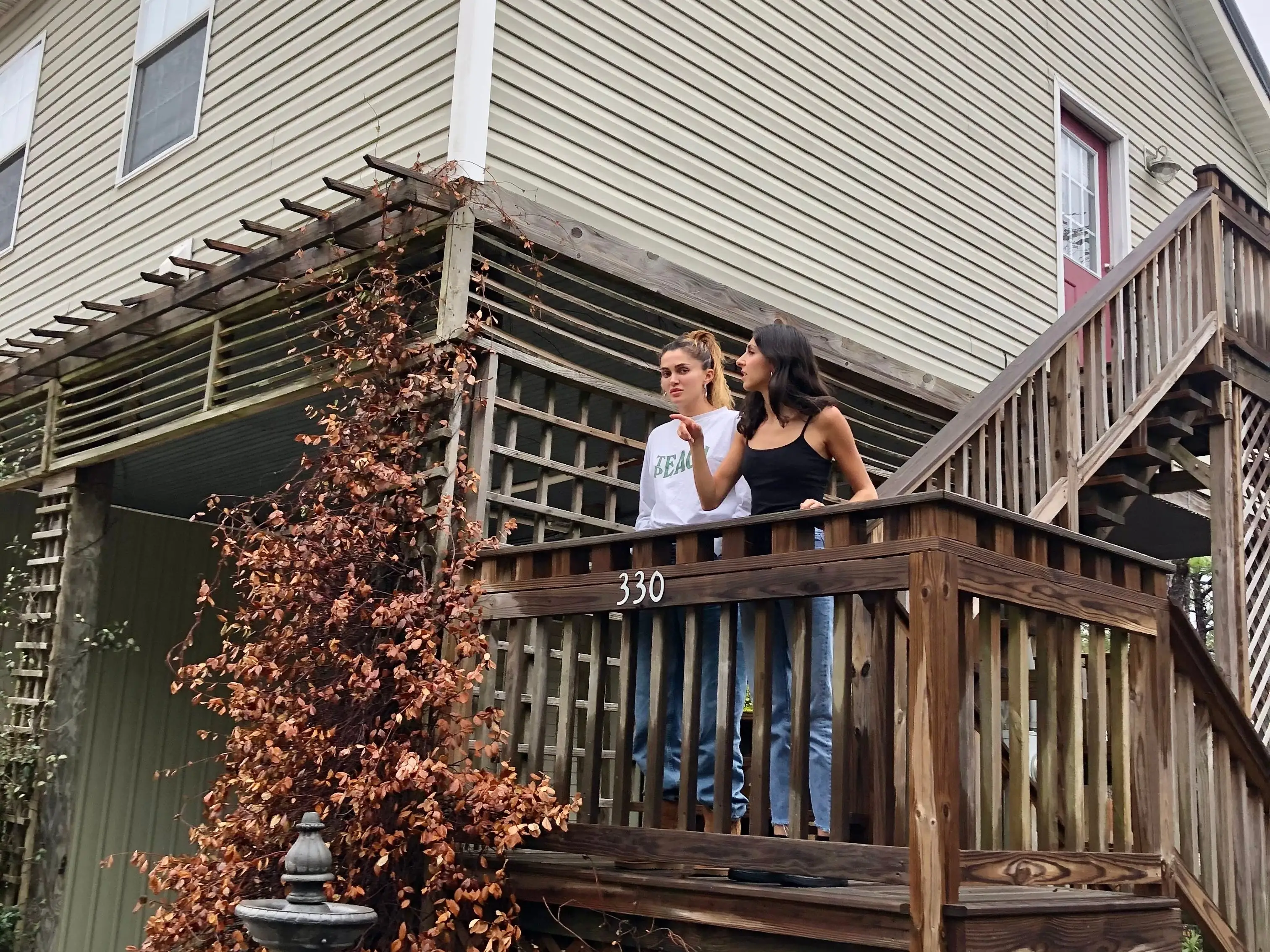 Two women stand on the stairs of a large two-story home.