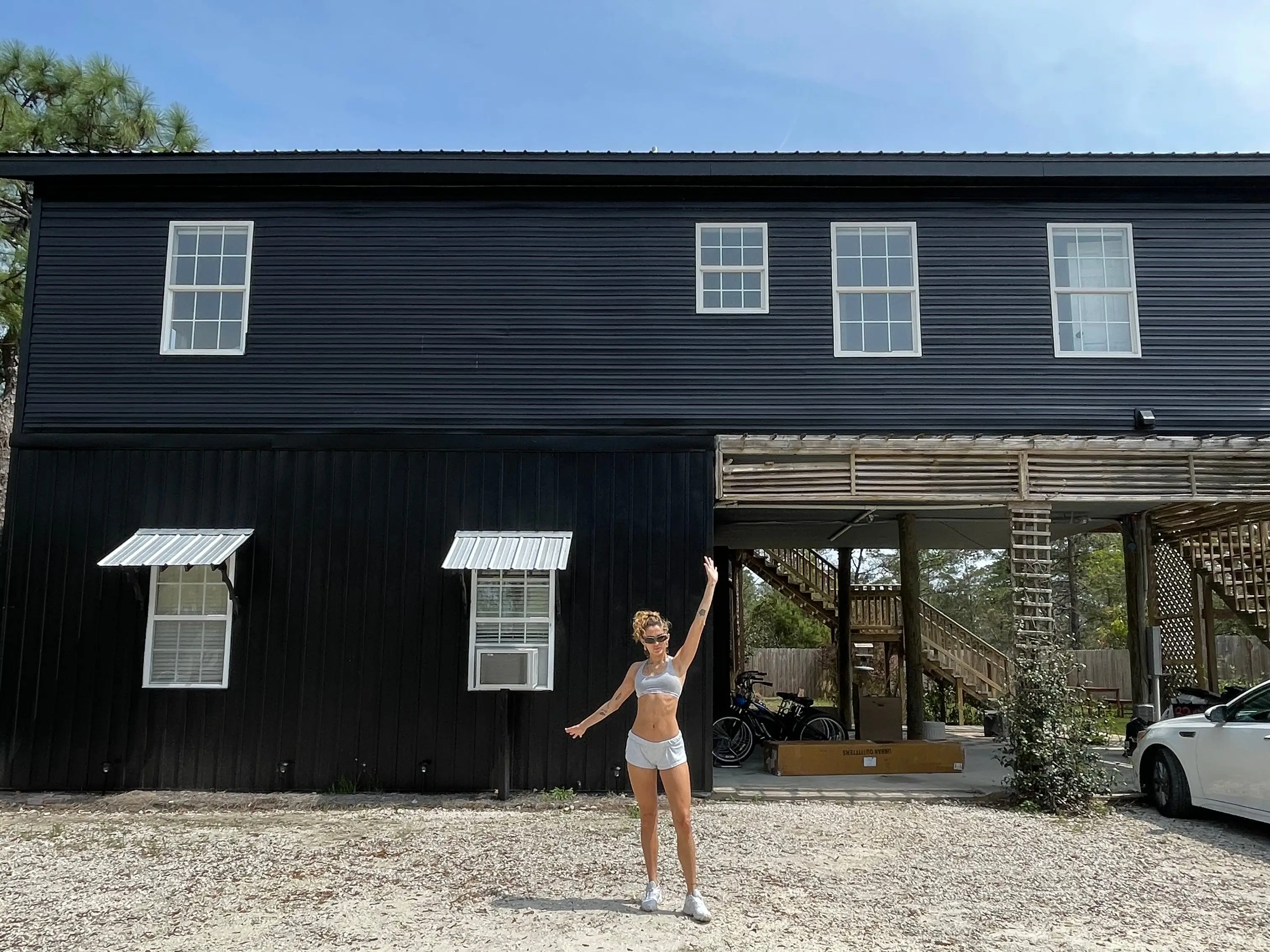 A woman stands with her arms wide open in front of a two-story home.