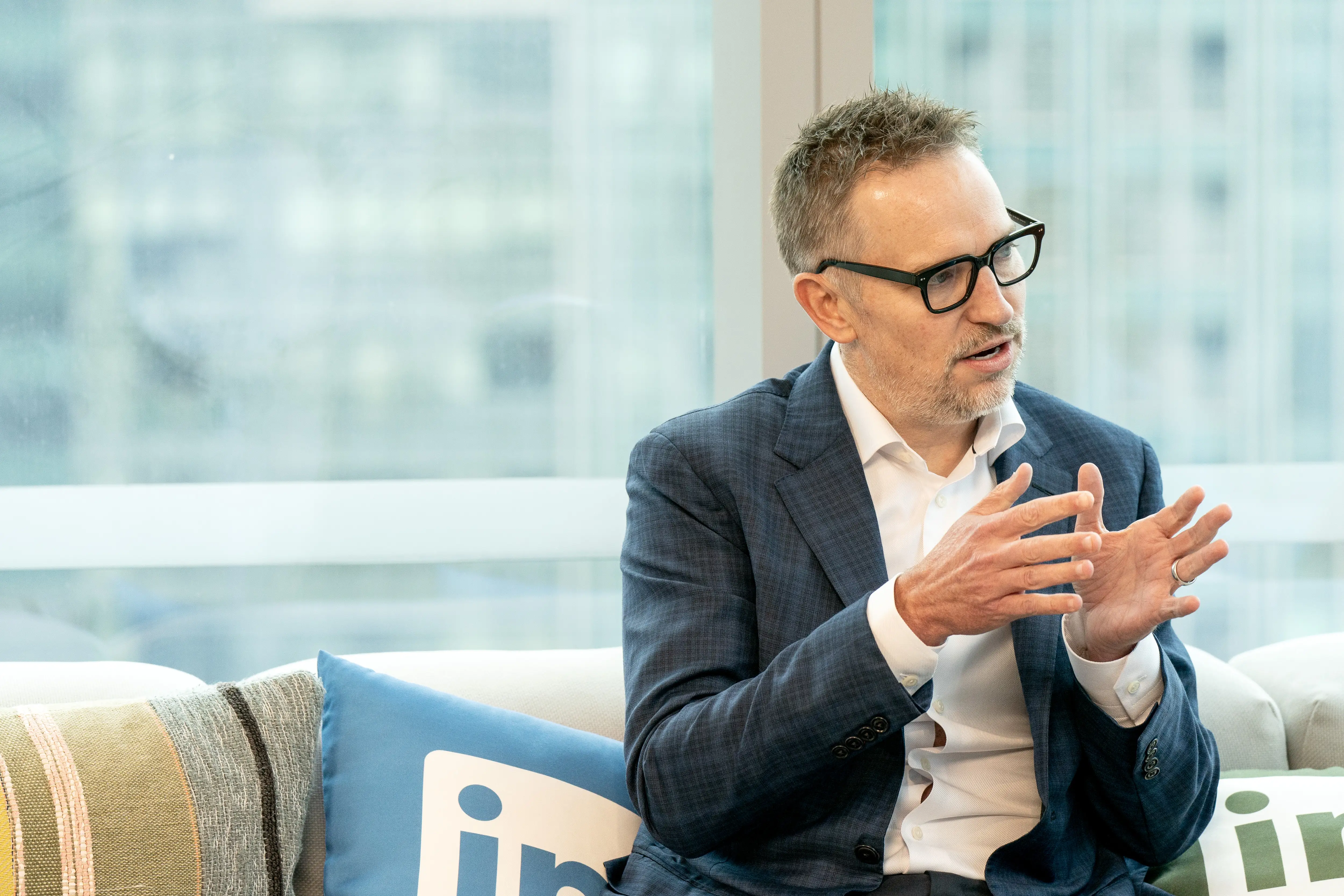 Ryan Roslansky, the LinkedIn CEO, is sitting on a couch with throw pillows decorated with the company's logo.