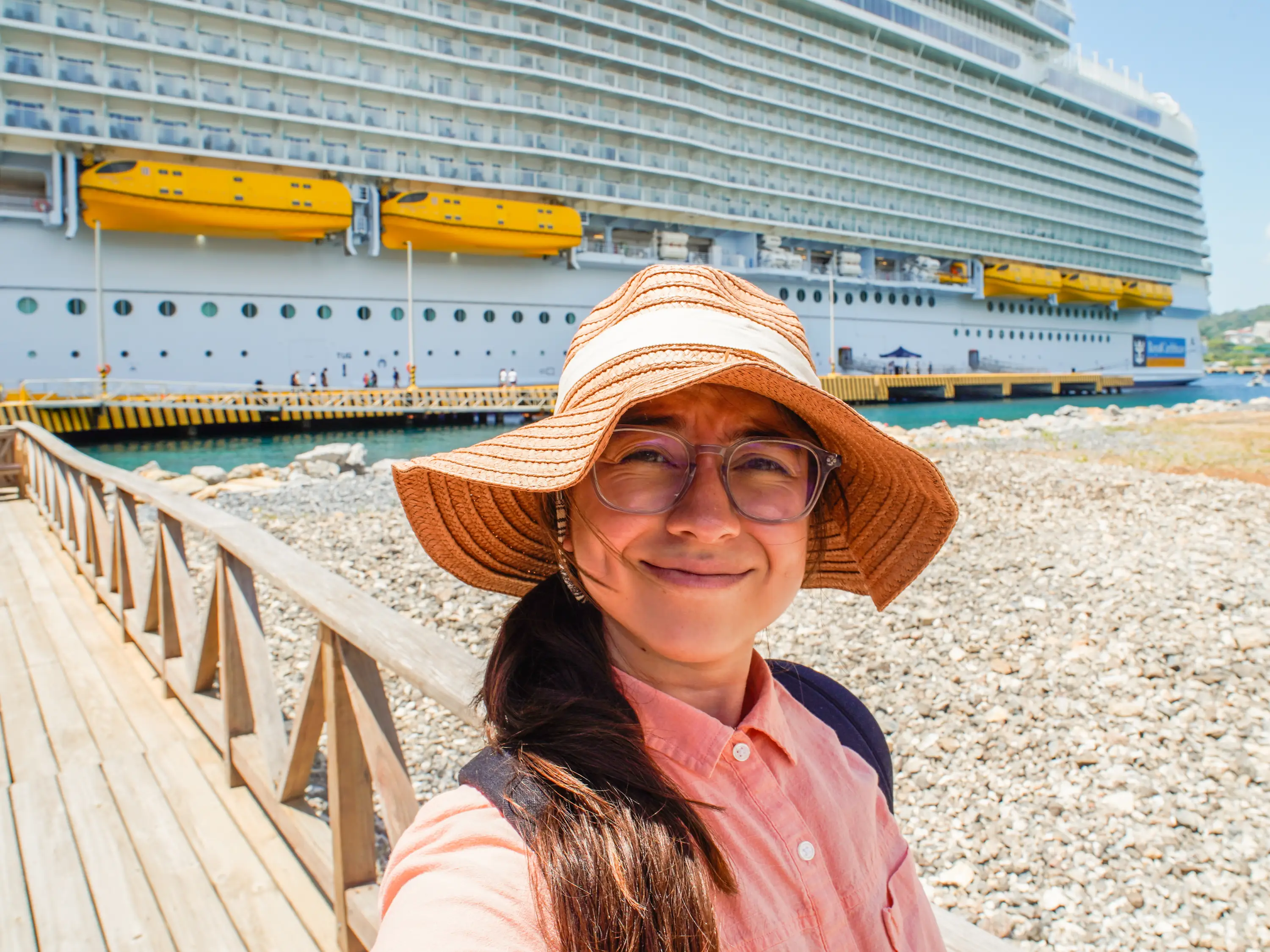 The author smiles in a sunhat in front of a cruise ship.