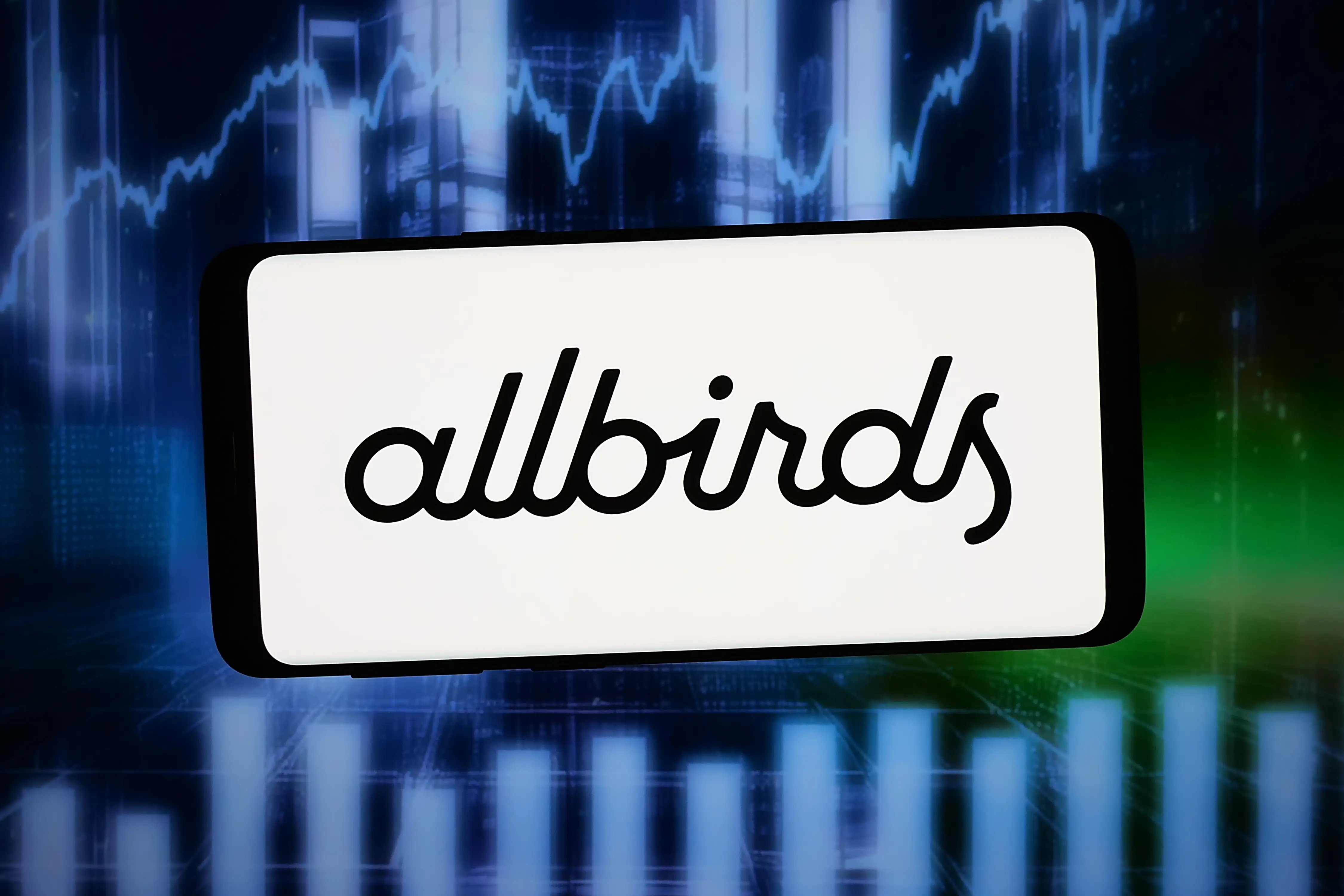 In this photo illustration, the logo of footwear company Allbirds Inc. is displayed on a smartphone in front of abstract background on computer screen.