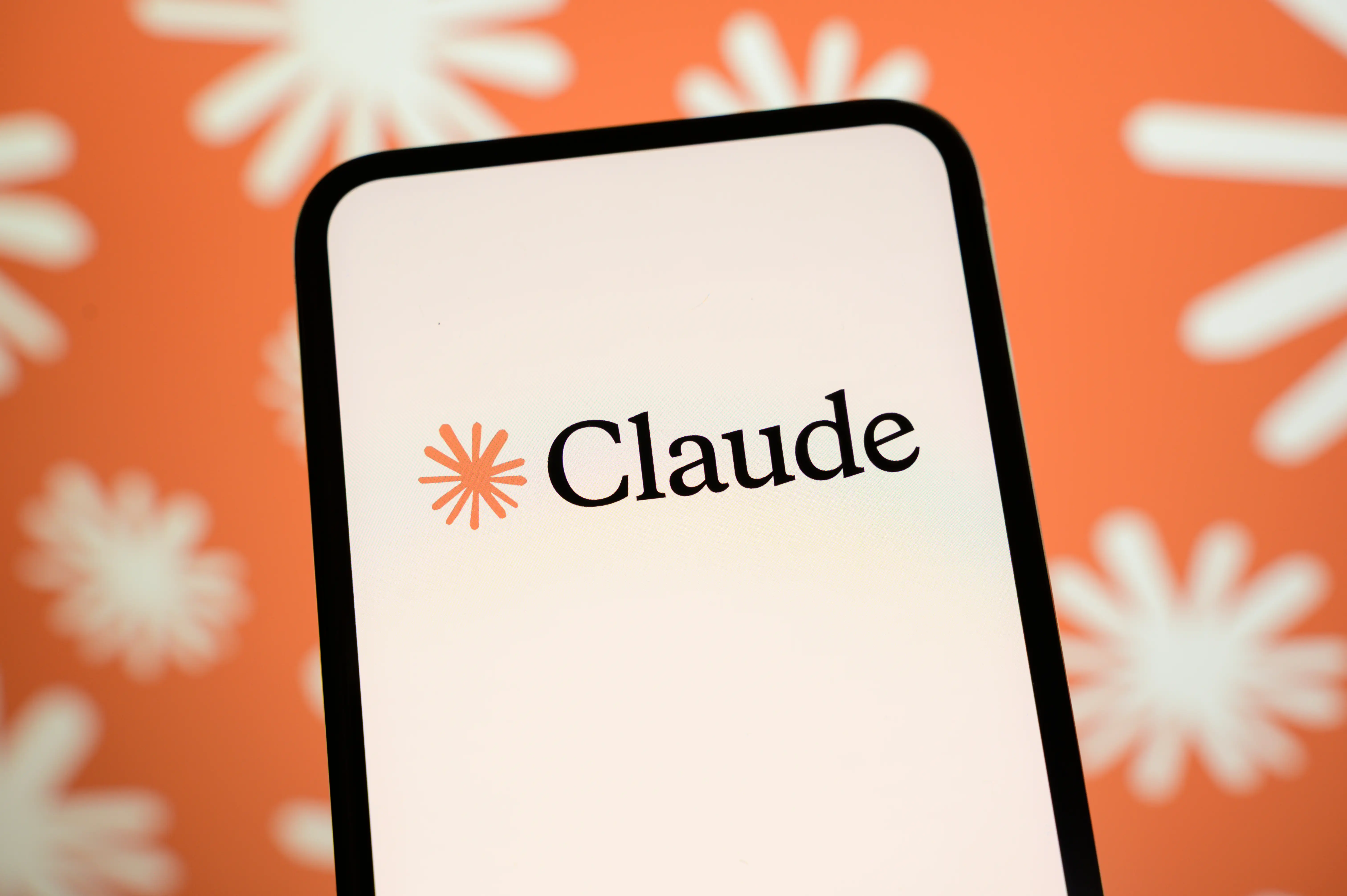 A phone displaying the Claude logo from Anthropic is pictured.