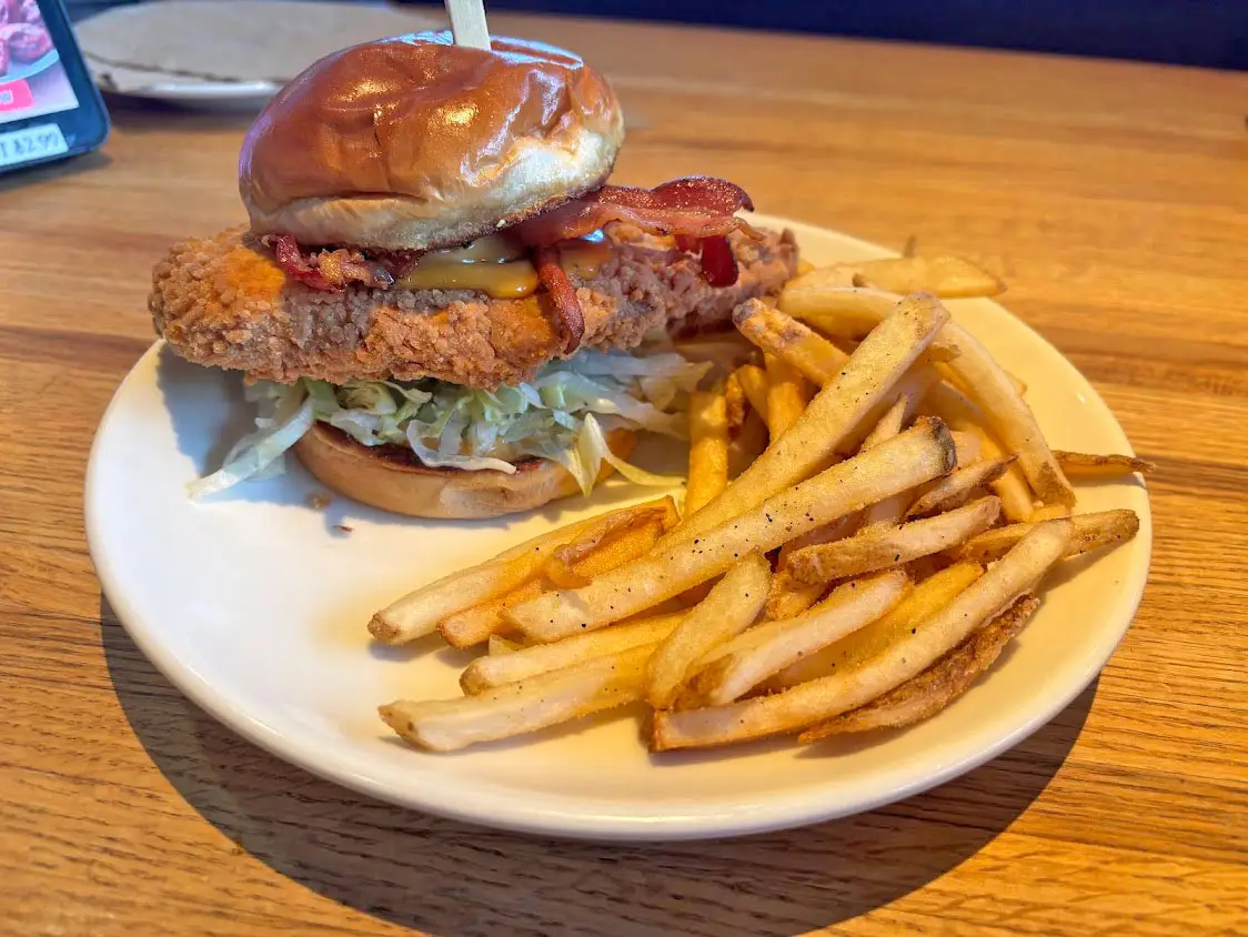 A chicken sandwich with bacon and lettuce on a white plate with fries.