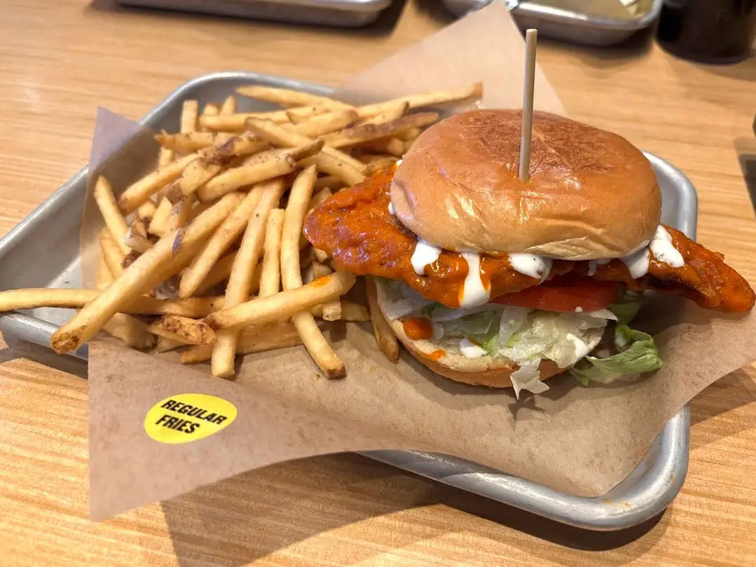 A Buffalo chicken sandwich with lettuce on a metal tray with fries.