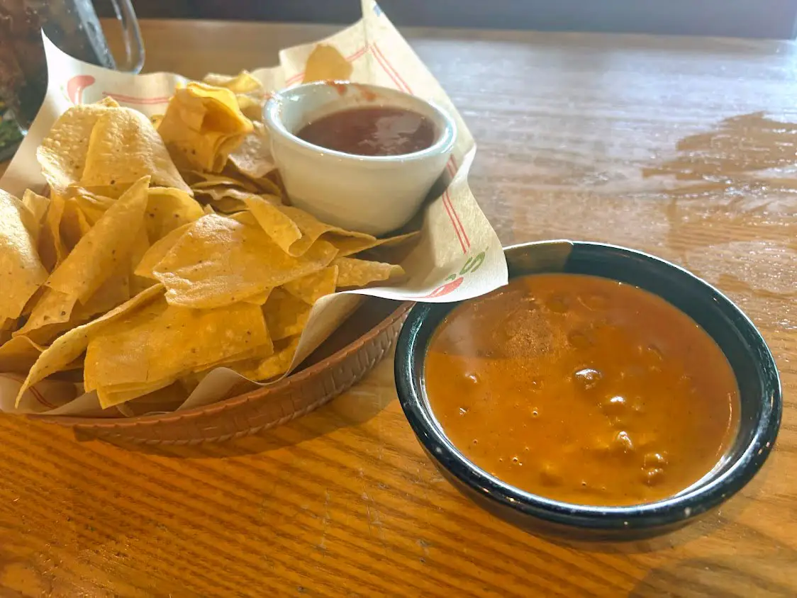 A basket of chips and salsa and a bowl of queso on a table.