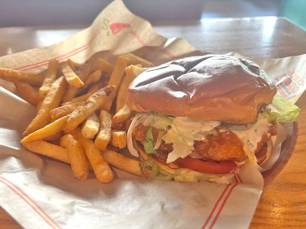 A breaded chicken sandwich with lettuce and tomato in a basket with fries.