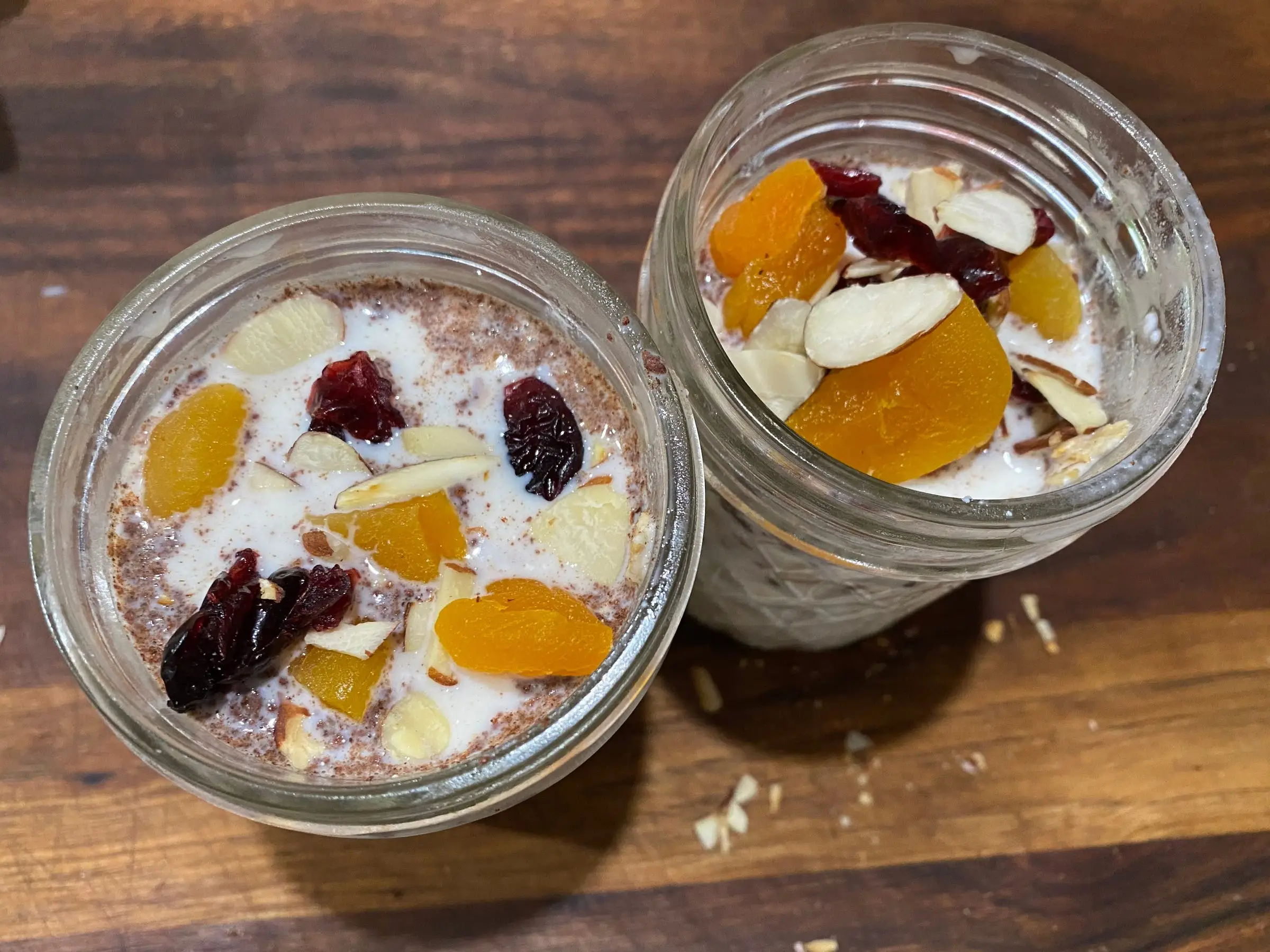 two jars with overnight oats, milk, topped with dried fruits and sliced almonds