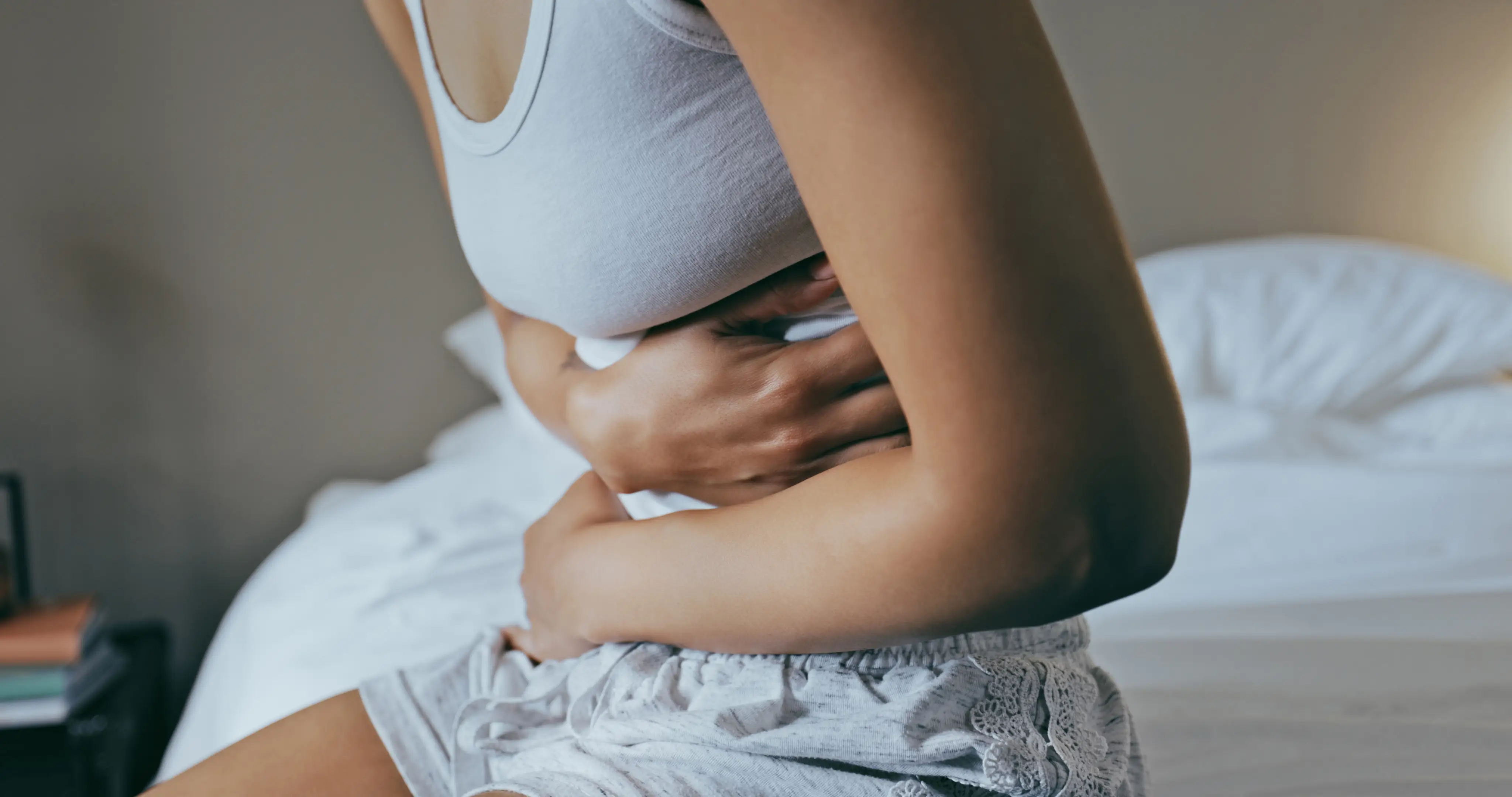 A young woman holding her stomach, sitting in bed with abdominal cramps.