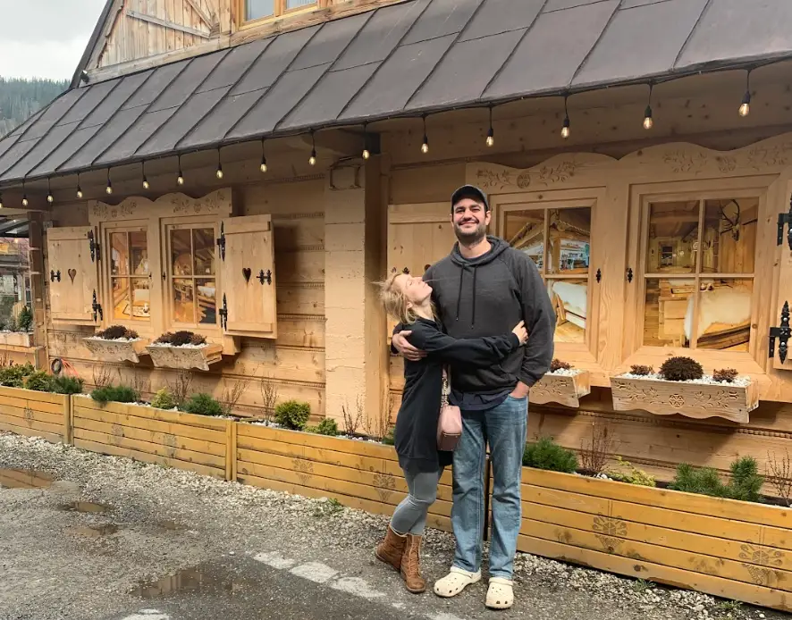 The writer hugging her husband in front of a wood house.