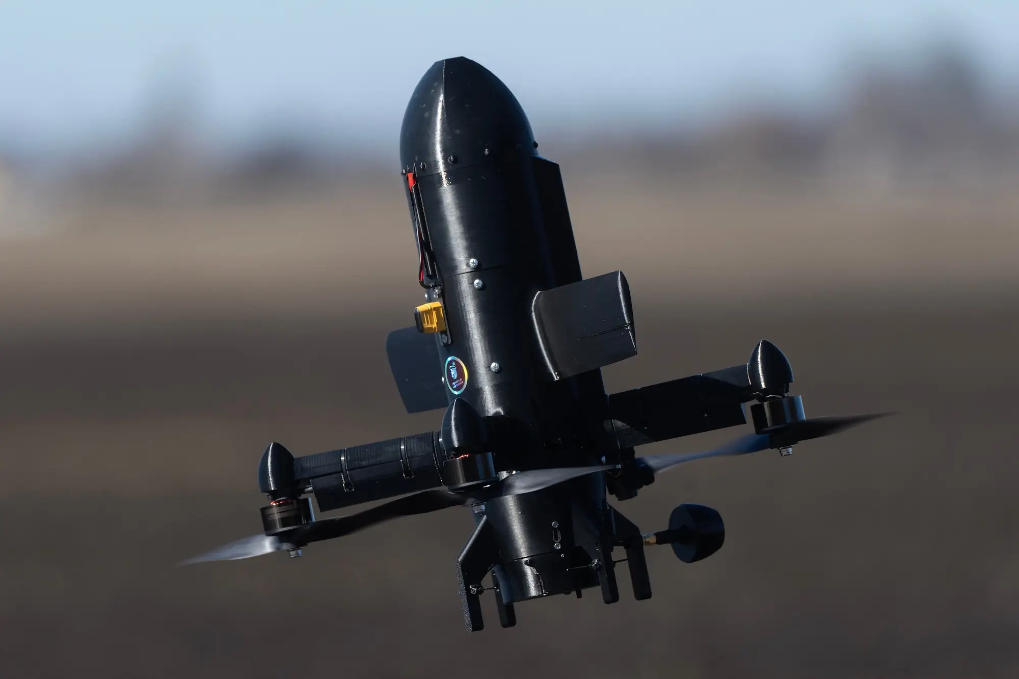 A black bullet-shape interceptor drone in the sky with a blurred background