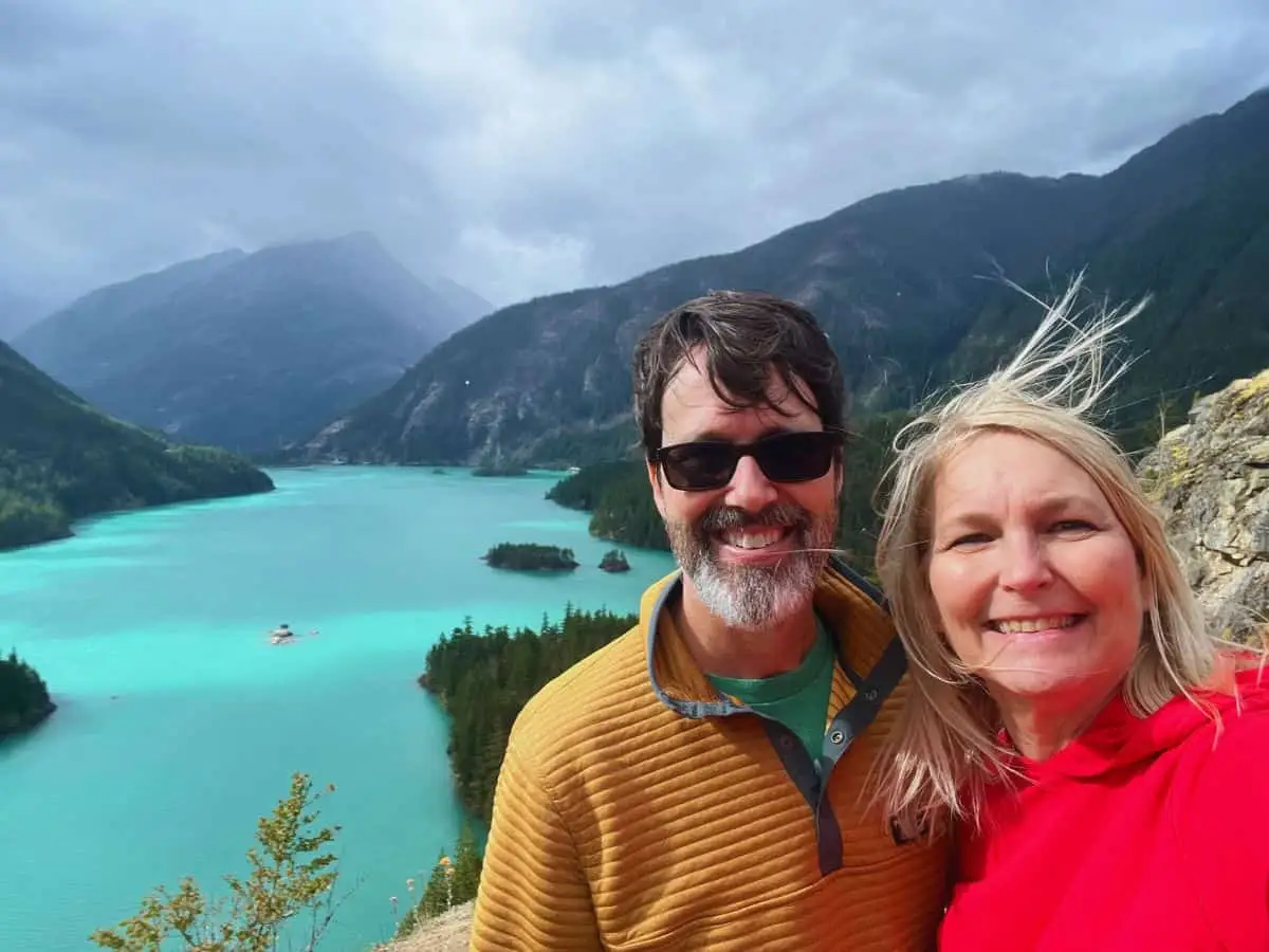 Scott and his wife stand in front of a turquoise lake surrounded by mountains in North Cascades National Park.